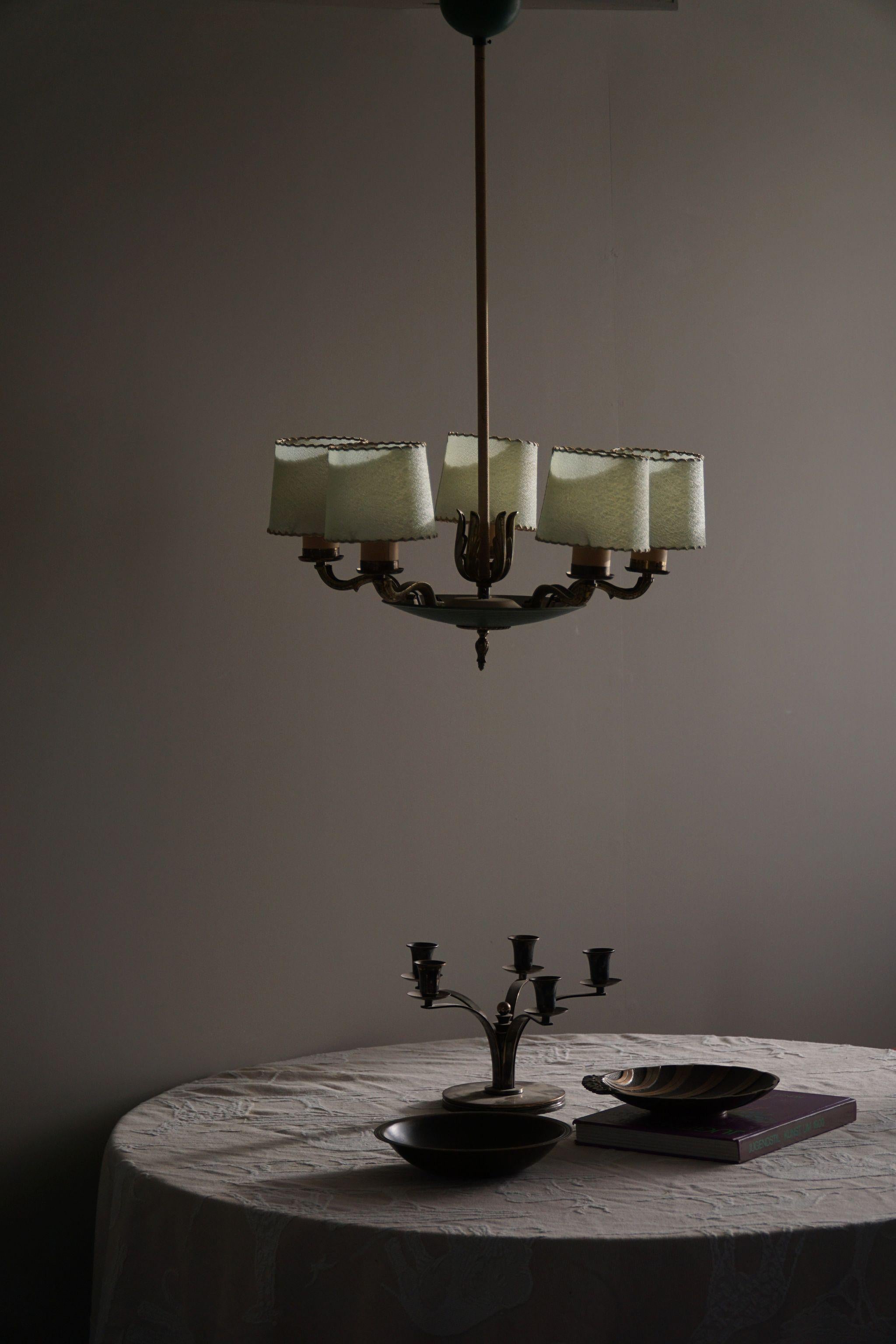 This exquisite chandelier, crafted in the 1930s by the renowned Finnish designer Paavo Tynell for Taito OY, emanates the 30s elegance and sophistication. Crafted from a blend of lustrous brass and sleek metal, it exudes a luxurious aura that