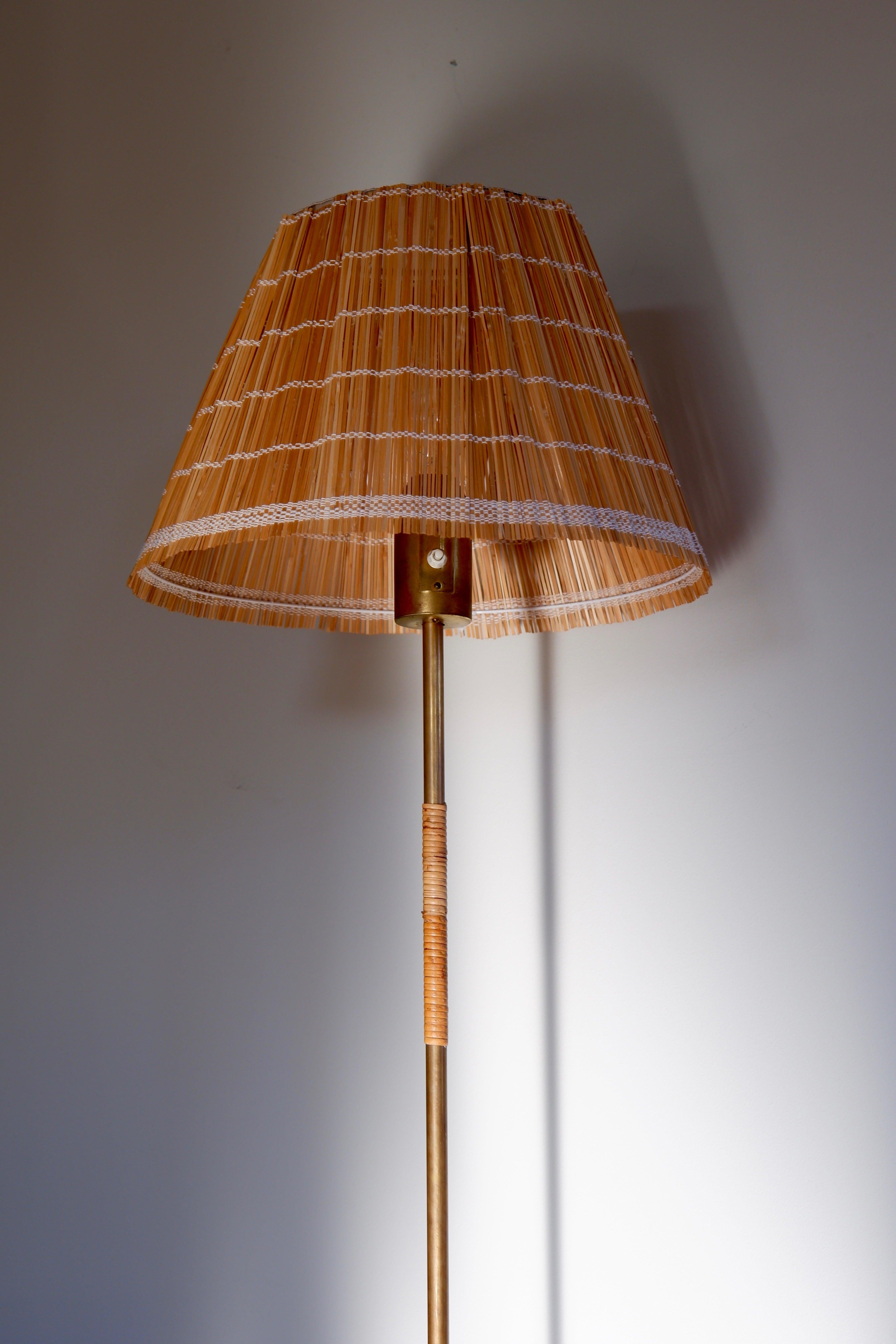 Beeindruckende Stehleuchte von Paavo Tynell, entworfen in den 50er Jahren und hergestellt von IDMAN. Die Leuchte hat einen Messingfuß, einen Kern und einen Kopf mit einem einzelnen Lichtschalter auf der Oberseite. Der Messingkern ist mit Rattan