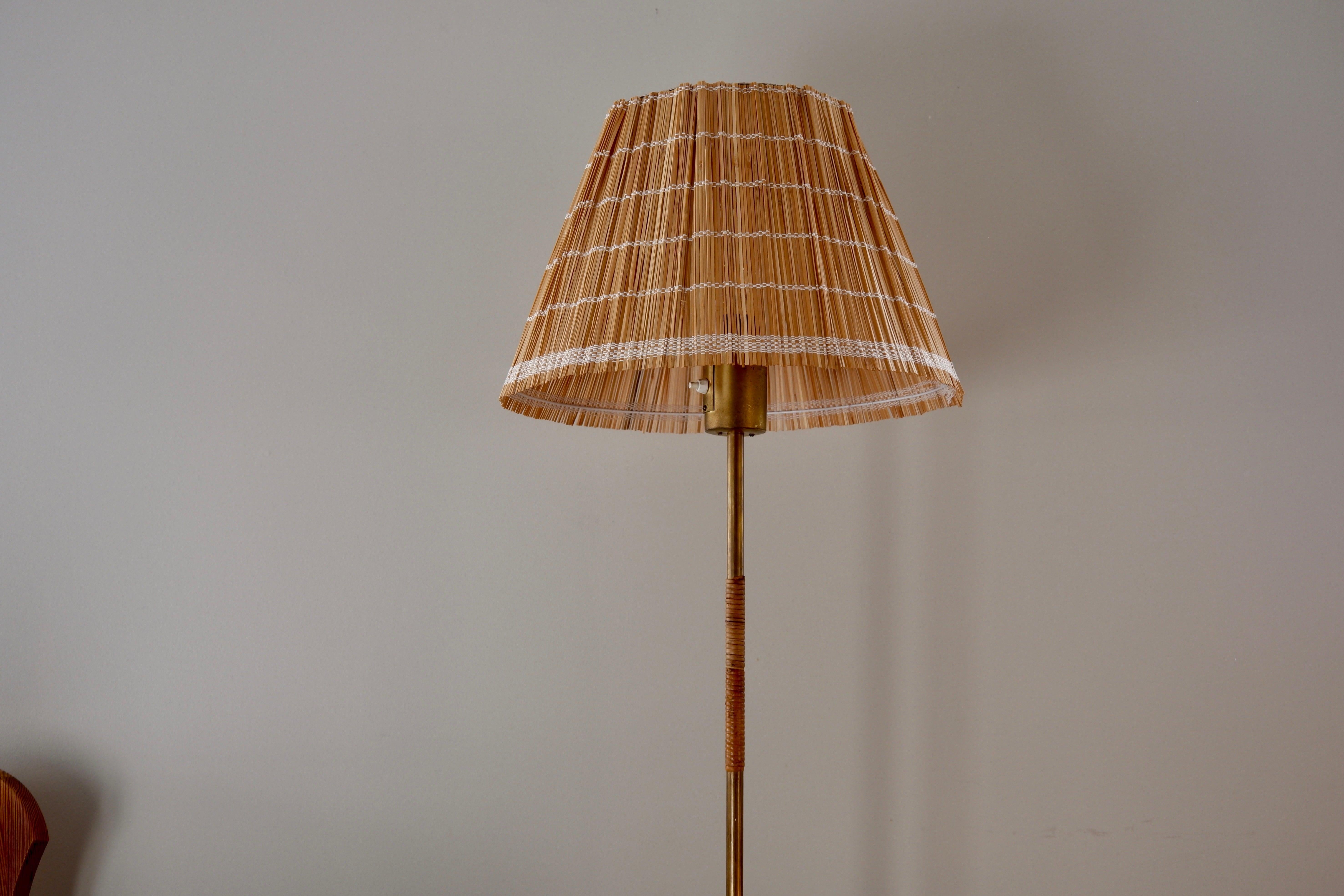 Impressive Paavo Tynell floor lamp design in the 50's and produced by IDMAN. The fllor lamp has a brass feet, core and head with a single lighting switch on top. the brass core is decorated with rattan which is orginal. The lamp is stamp by the