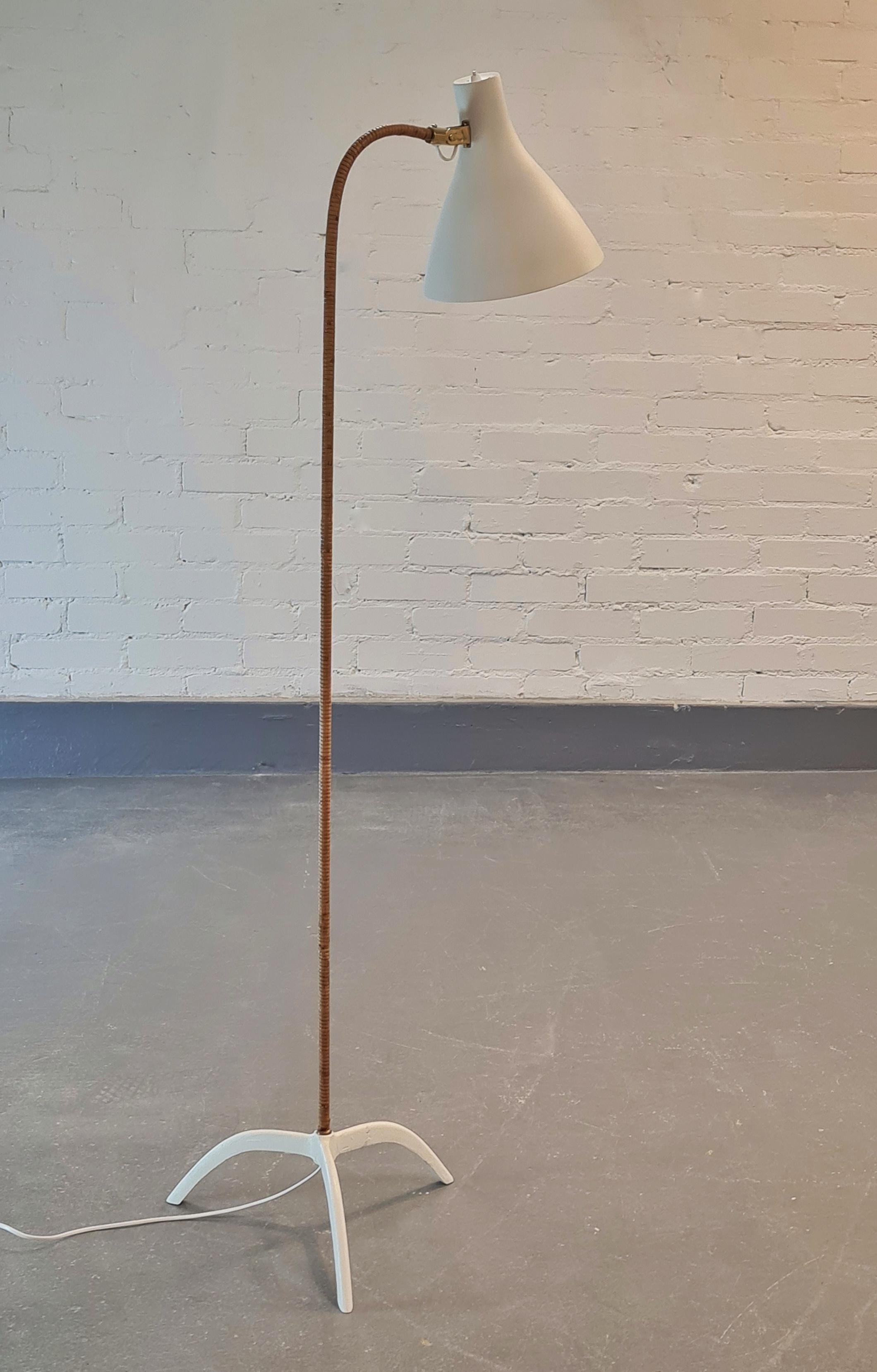 This Paavo Tynell floor lamp model number 9603 is from 1950's. 
It has a wide, white repainted funnel shape aluminum shade, diameter 25 cm, with a switch button. The shade is reversible. The light color rattan stem, which is curved from the top is