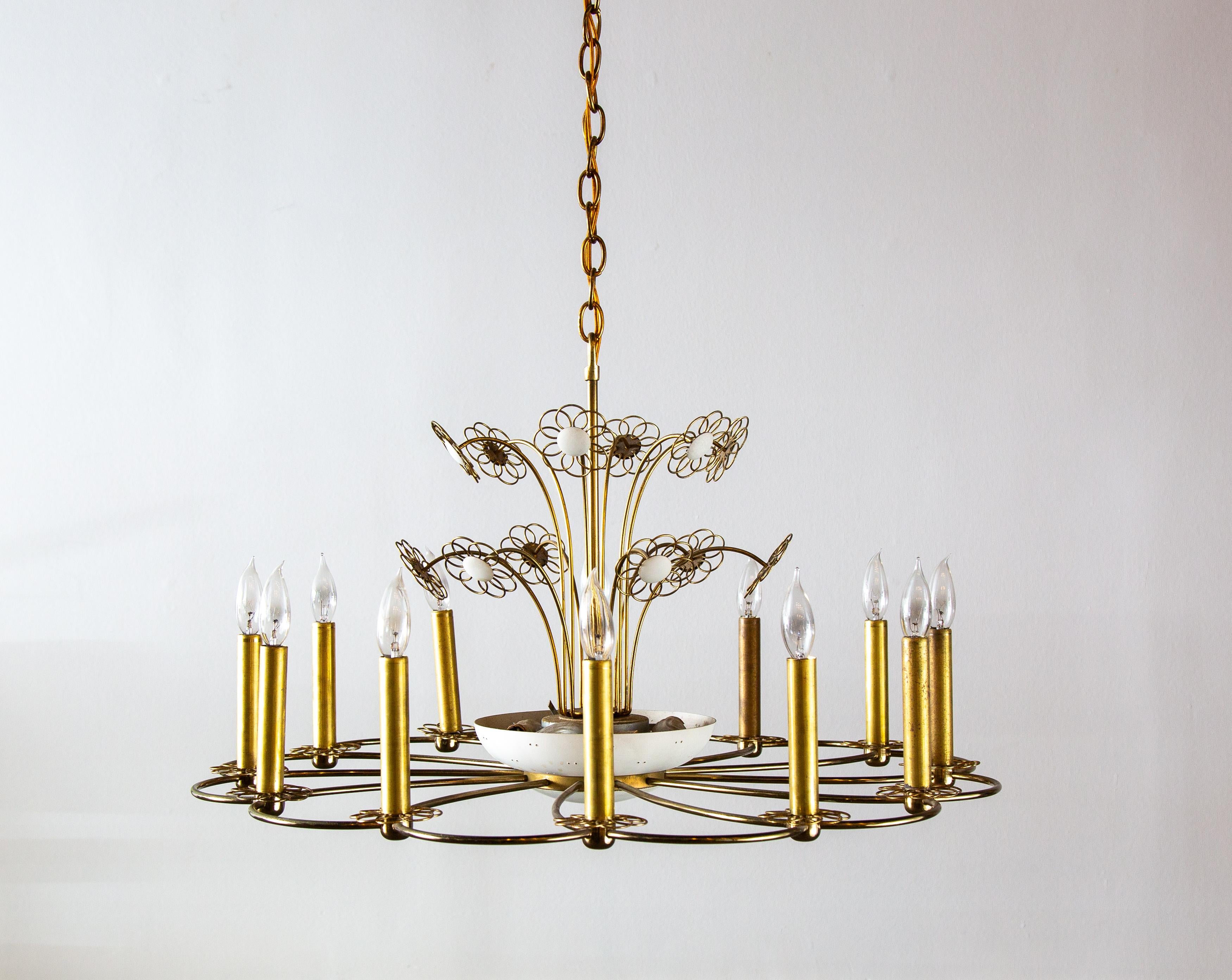 A 1960s chandelier designed by Paavo Tynell for Lightolier. 12 Candelabra bulbs around the circumference accentuated with brass wire flowerlets at the bottom of each. From underneath the brass frame features a swirling pattern.  The center includes