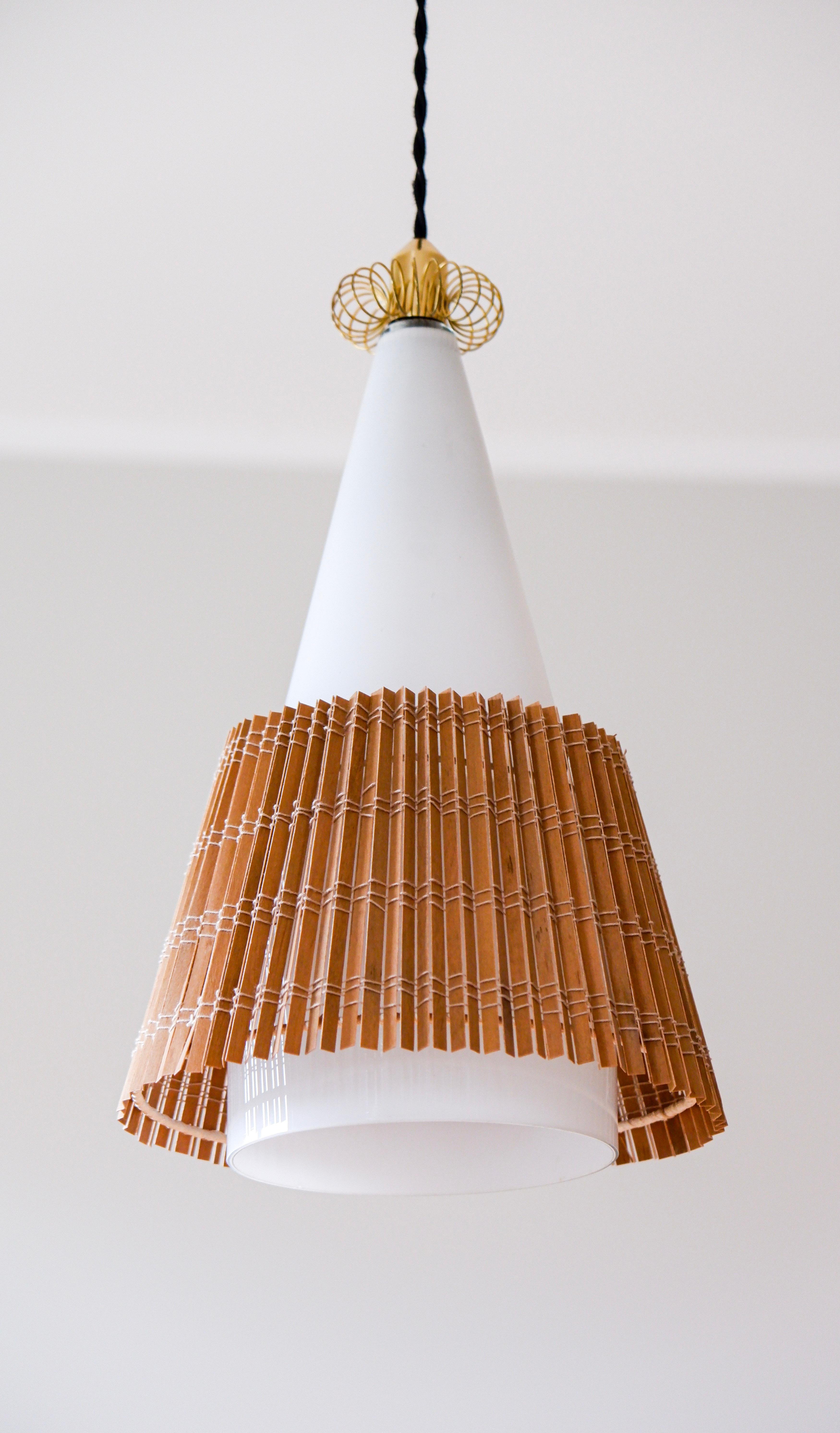 Suspension modèle 1082 conçue par Paavo Tynell pour Idman, la lampe est composée d'un verre opale avec une décoration en laiton et son abat-jour original en rotin. La lampe est en bon état dans son ensemble. Paavo Tynell est l'un des principaux