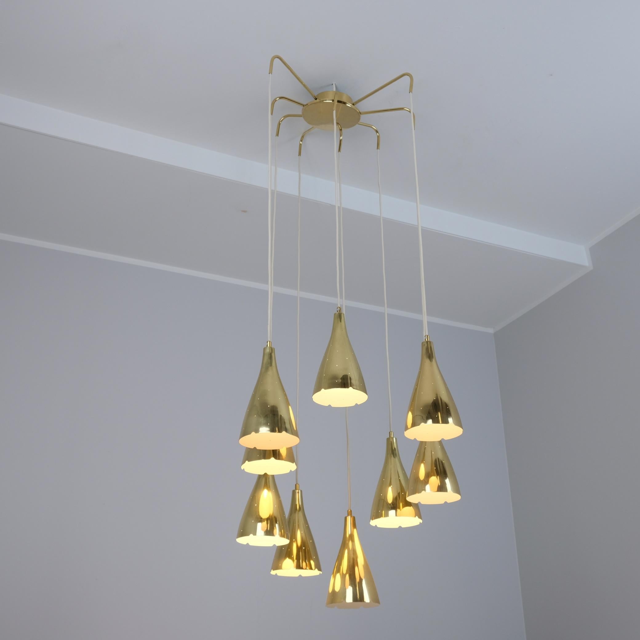 A sizable ceiling light by Paavo Tynell with nine hanging perforated brass pendants connected at the top with a brass central piece with radiating arms of different lengths. The pendants themselves hang at different heights and can also be adjusted