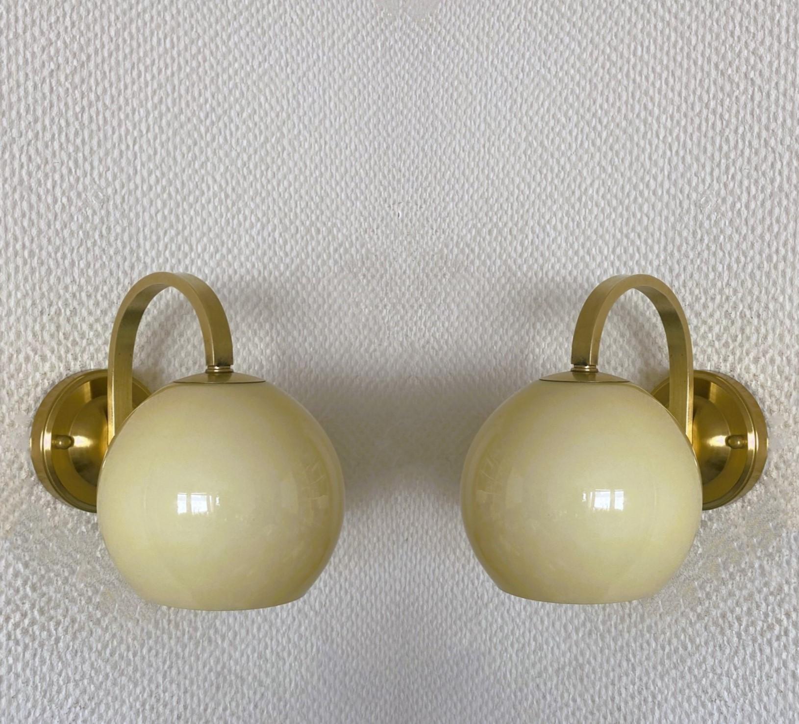 A pair of brass and glass wall lights attributed to Paavo Tynell, Finland, 1950s. Clean lines design from the Scandinavian Modern period, opaline glass shades in cream color. In good vintage condition, no damages, brass with some wear and aging