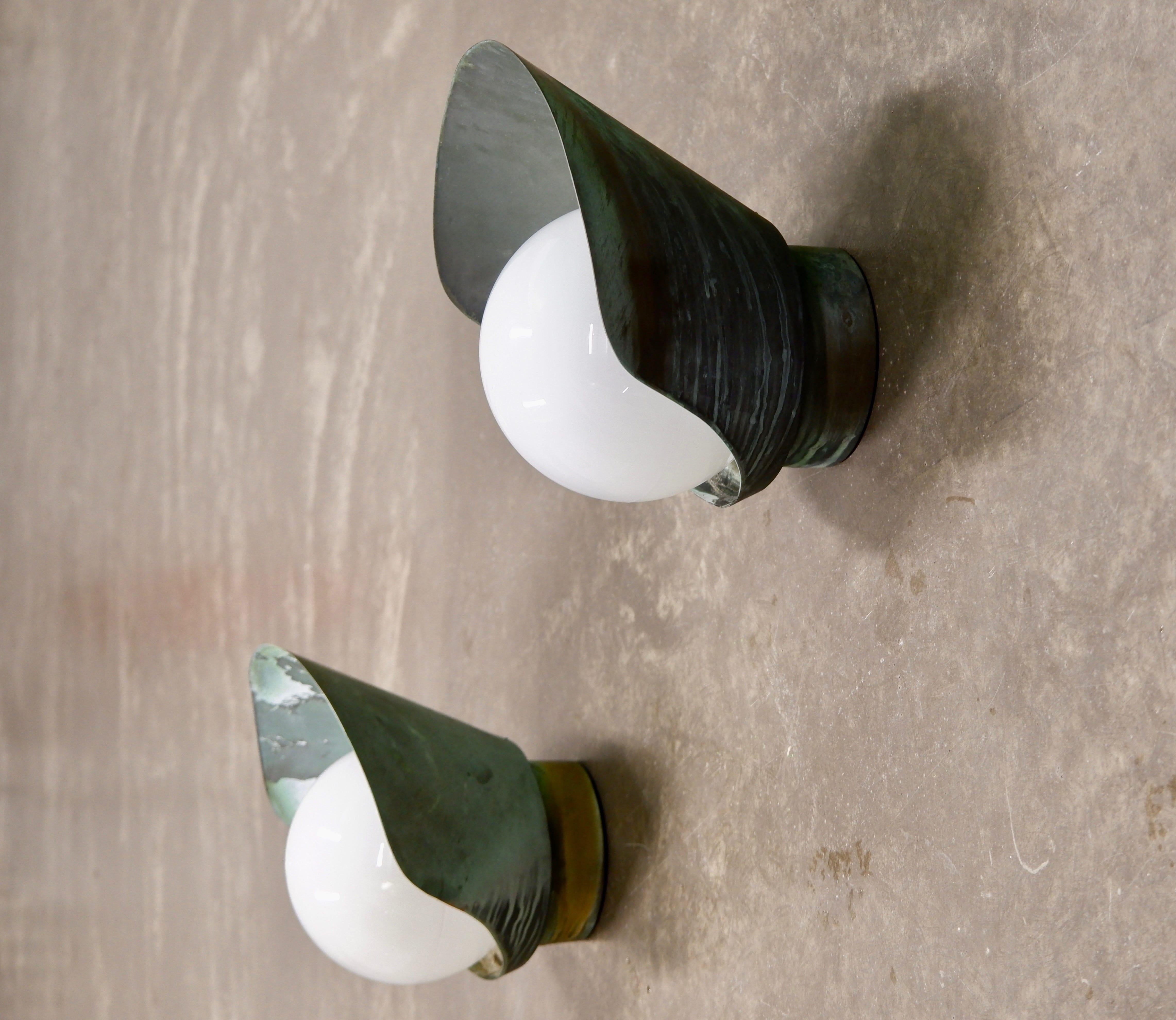 Patiniertes und schönes Paar Paavo Tynell Wandlampen aus Kupfer und hergestellt von TAITO oy in den 1940er Jahren. Die Lampen sind beide mit einem massiven, kupferfarbenen Schirm versehen und haben in der Mitte eine runde Opaline. Beide Lampen
