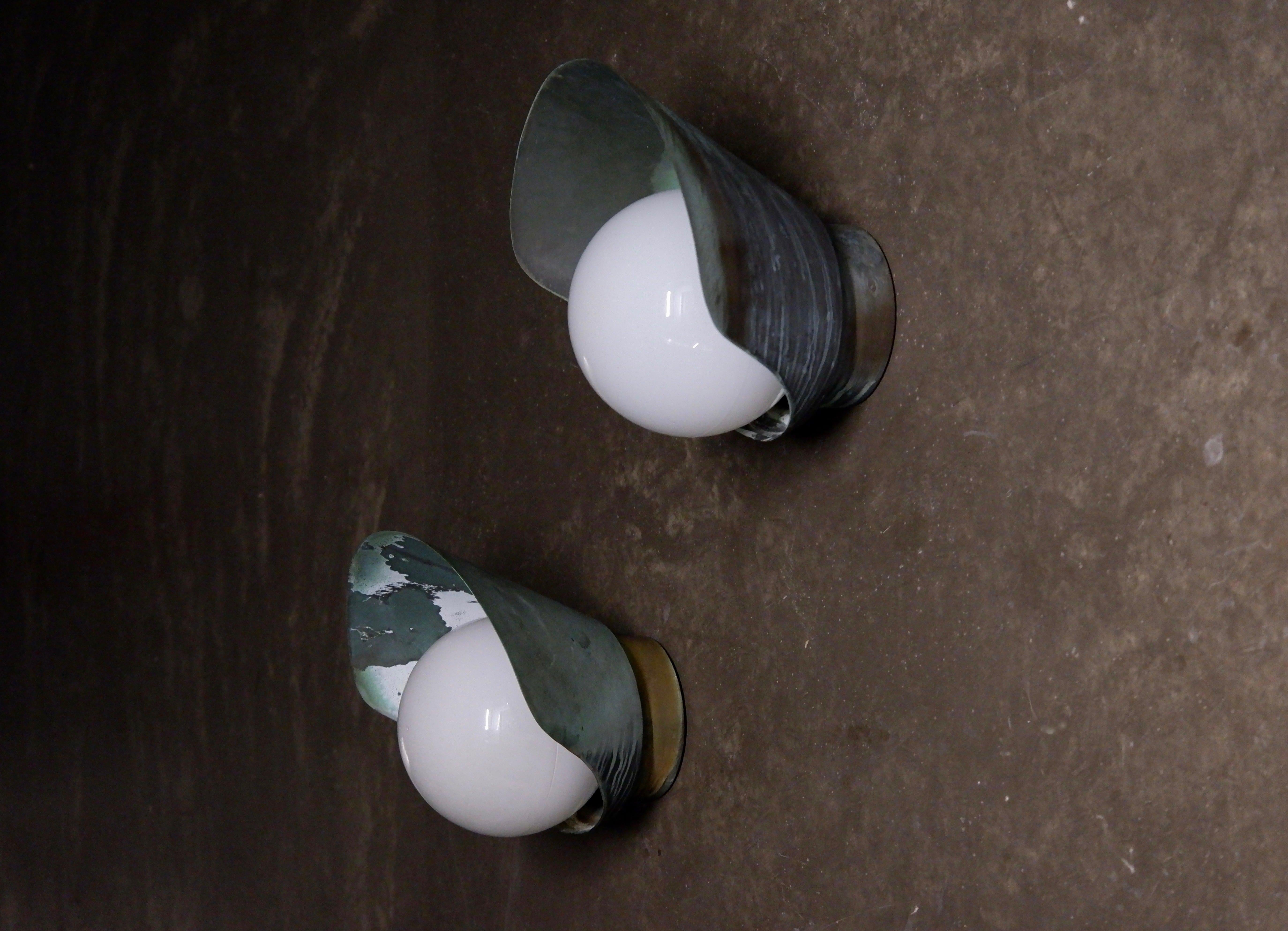 Bella coppia di lampade da parete Paavo Tynell patinate e realizzate in rame e prodotte da Taito Oy negli anni Quaranta. Entrambe le lampade sono realizzate con un solido paralume in cocco e hanno un'opalina rotonda al centro. Entrambe le lampade