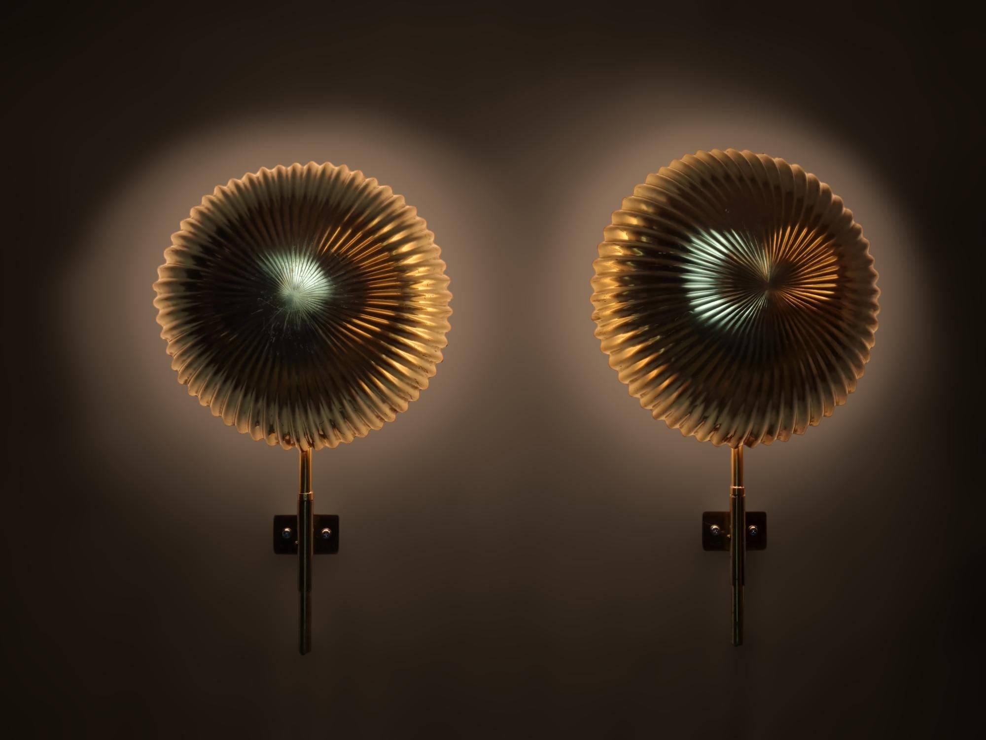 A pair of large, commissioned, and extremely rare Seashell wall lamps, designed by Paavo Tynell and manufactured by Taito in Finland in the early 1950s. Each lamp features a lightbase behind the shell shaped shade with an adjustable brass stem. The