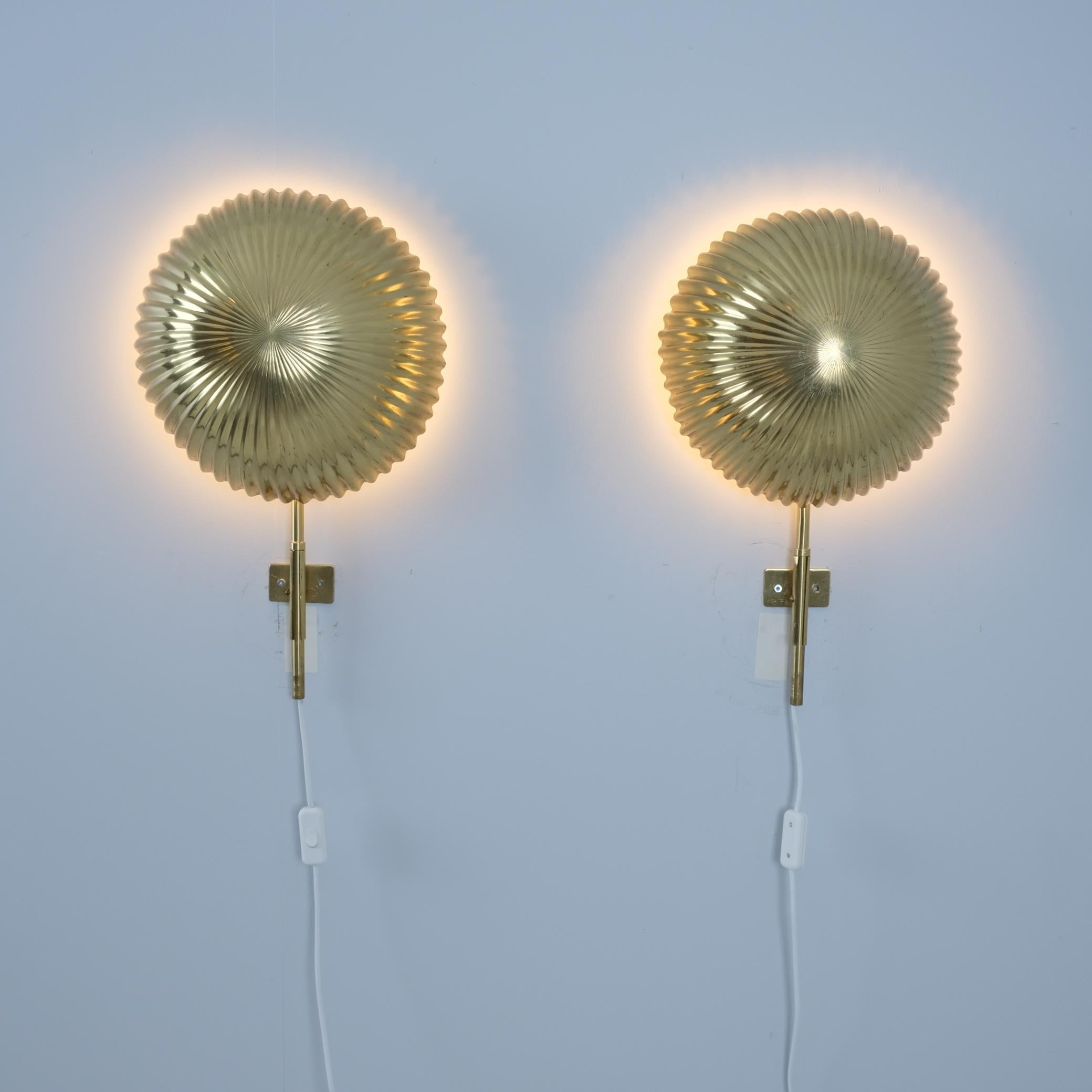 A pair of large, commissioned, and extremely rare Seashell wall lamps, designed by Paavo Tynell and manufactured by Taito in Finland in the early 1950s. Each lamp features a lightbase behind the shell shaped shade with an adjustable brass stem. The