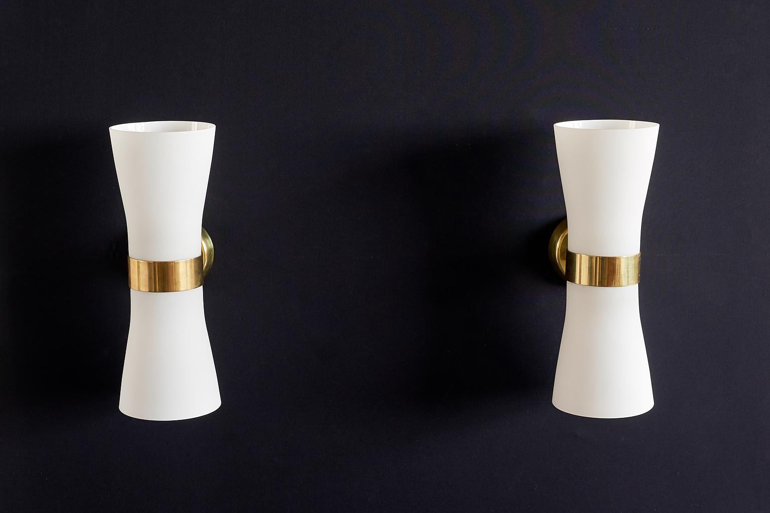 This rare pair of wall lights was designed by Paavo Tynell and produced by Idman in the early 1950s. They were designed for and used at the Governments Railway Station in Helsinki. The generously sized opaline glass shades are mounted on a brass