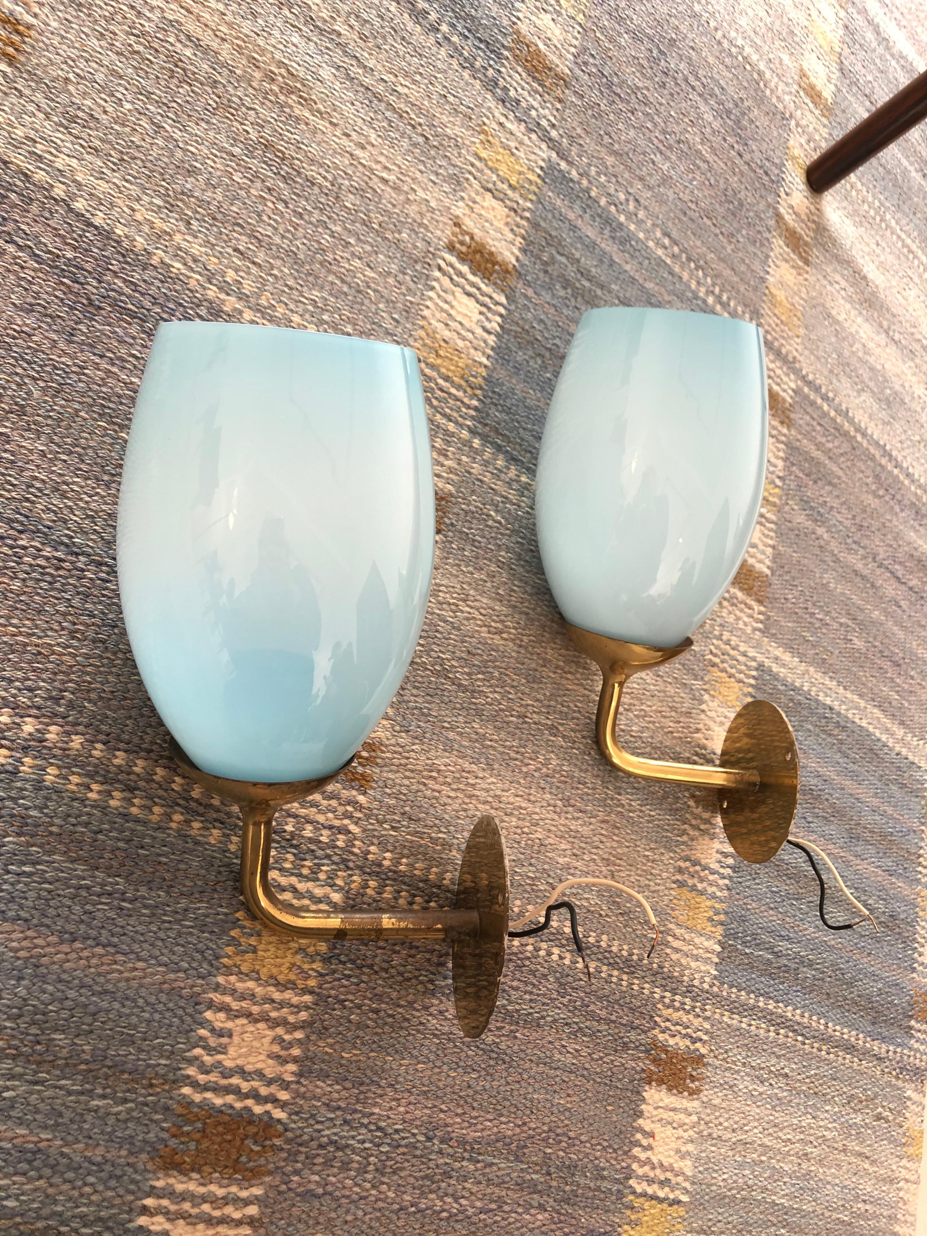 Pair of Paavo Tynell wall lights in brass and light blue glass for Taito Oy, Finland, 1940s.

Provenance: Kontiolax, Finland, 1940s.

Glass is in excellent condition with no chips or cracks.

Price is for the pair of lamps.