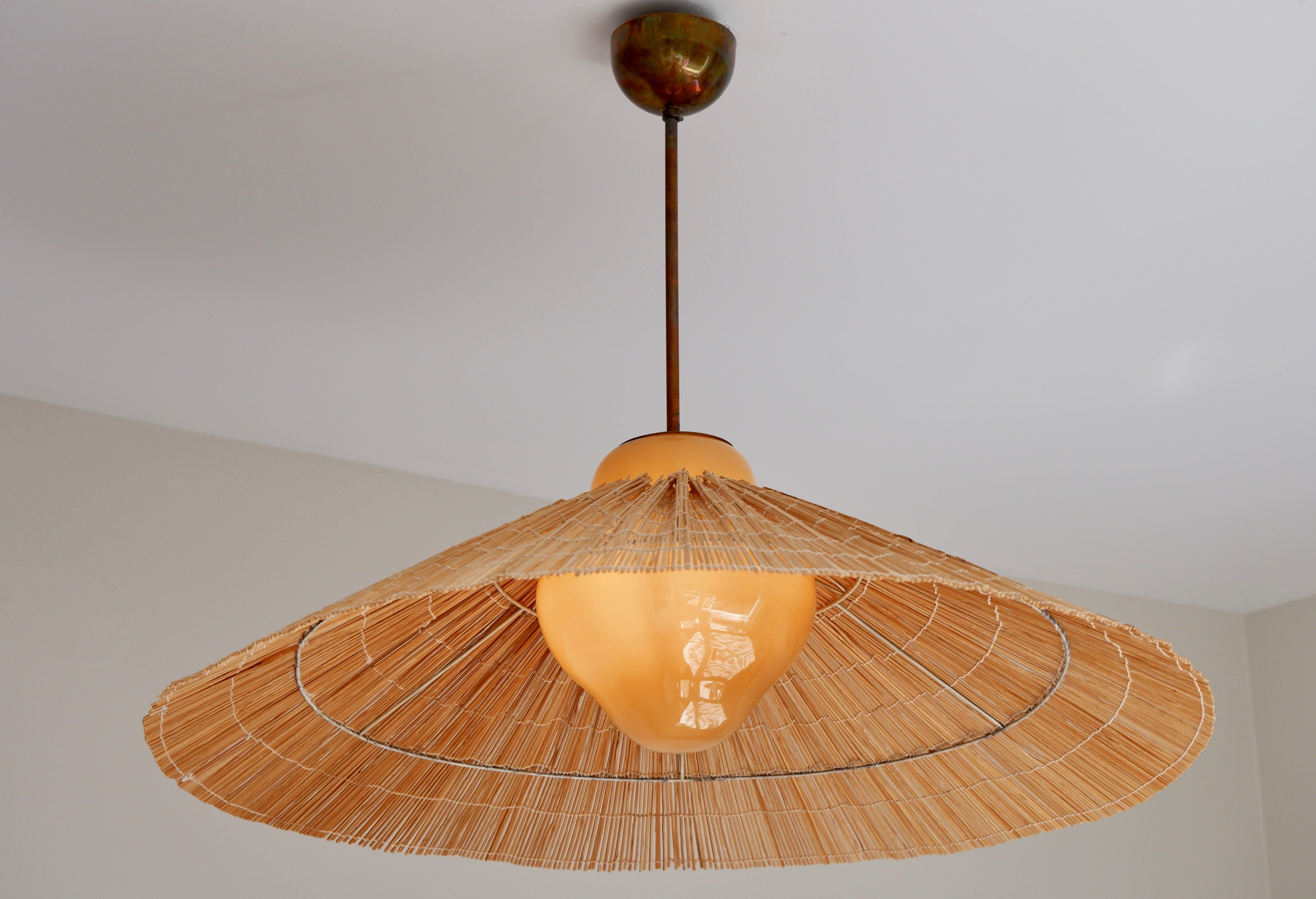 Impressive Paavo Tynell pendant model 1092/225 for TAITO design in the 40's and produced during this time in Tynell atelier. The lamp is hold by a brass core, and composed with a honey opal glass. The large shade is made with rattan and has been
