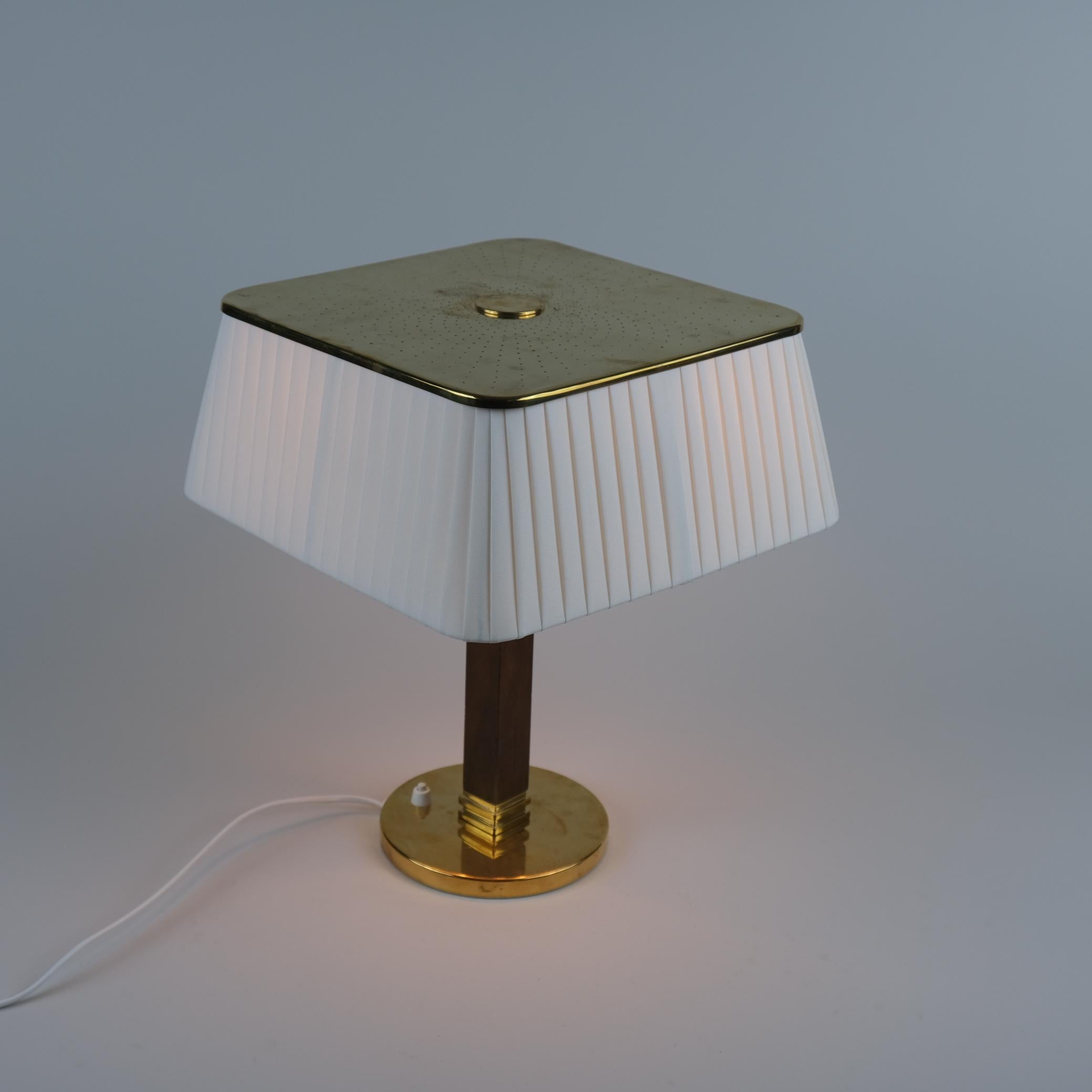 Lampe à poser modèle 5066 conçue par Paavo Tynell et fabriquée par Taito/One en Finlande dans les années 1950. Cette lampe est dotée d'un pied rond en laiton, d'une jambe en bois dur et d'un bel abat-jour en soie. L'abat-jour carré en laiton est