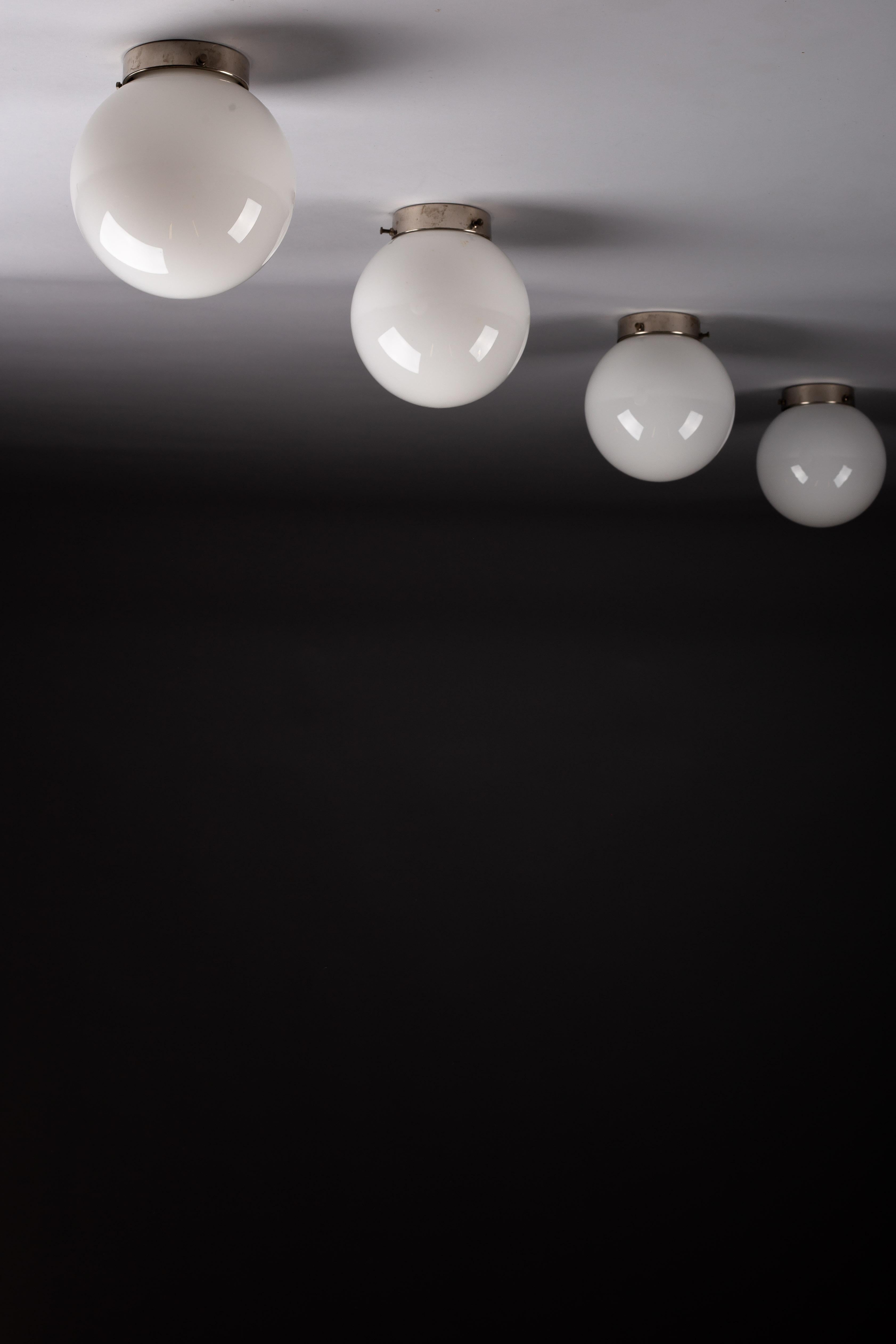 Illuminate your home with timeless elegance using this exquisite set of c. 1940's flush mounts by renowned designer Paavo Tynell, crafted by Taito Oy, Finland. These opaline glass sphere flush mounts are perfect for your ceiling or wall, breathing