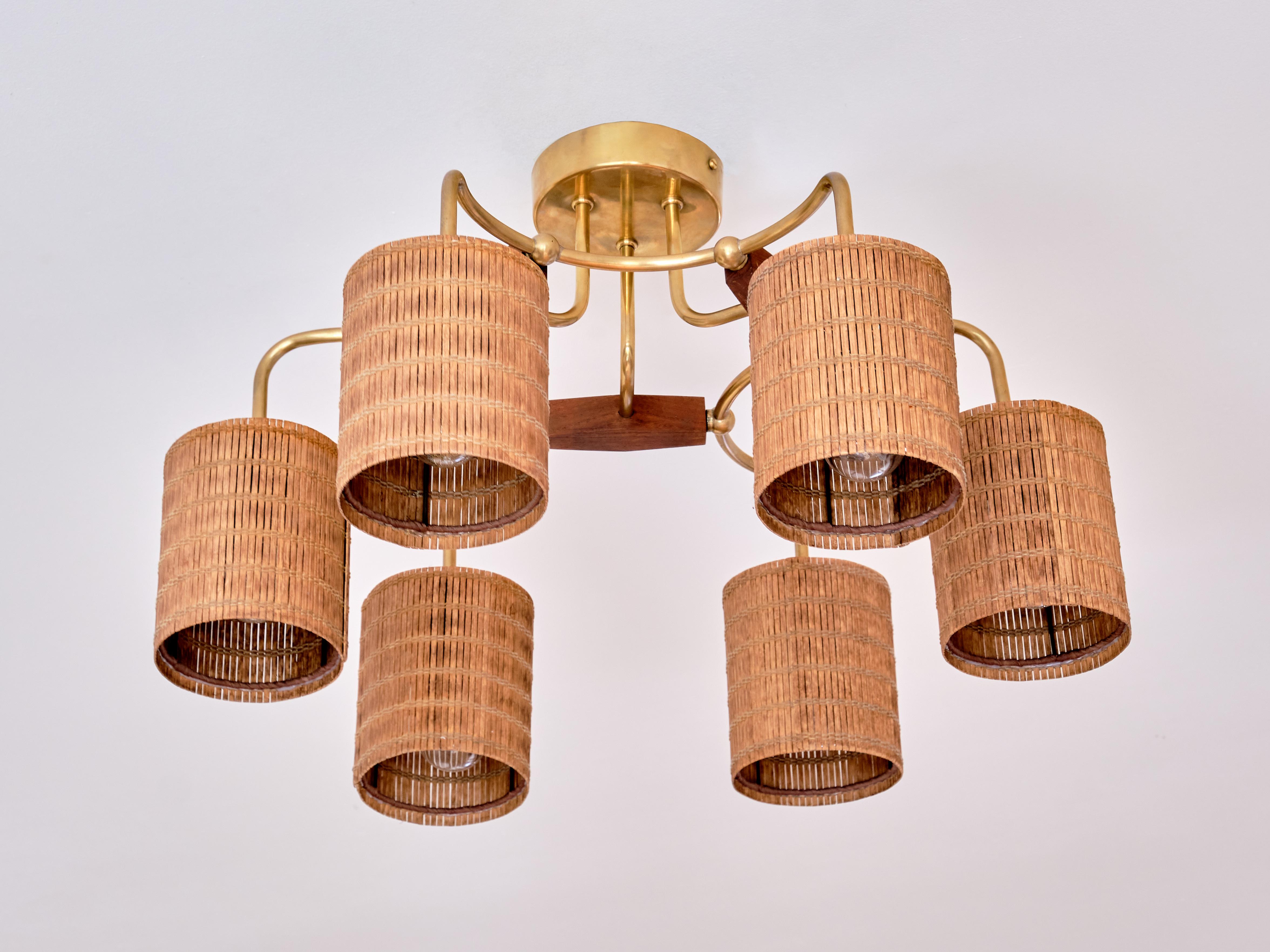This rare ceiling lamp was designed by Paavo Tynell and produced by Idman Oy in Finland in the 1950s. The brass fixture consists of six arms with six indivual lamp shades. Three teak wood elements connect the pairs of brass arms with the ceiling