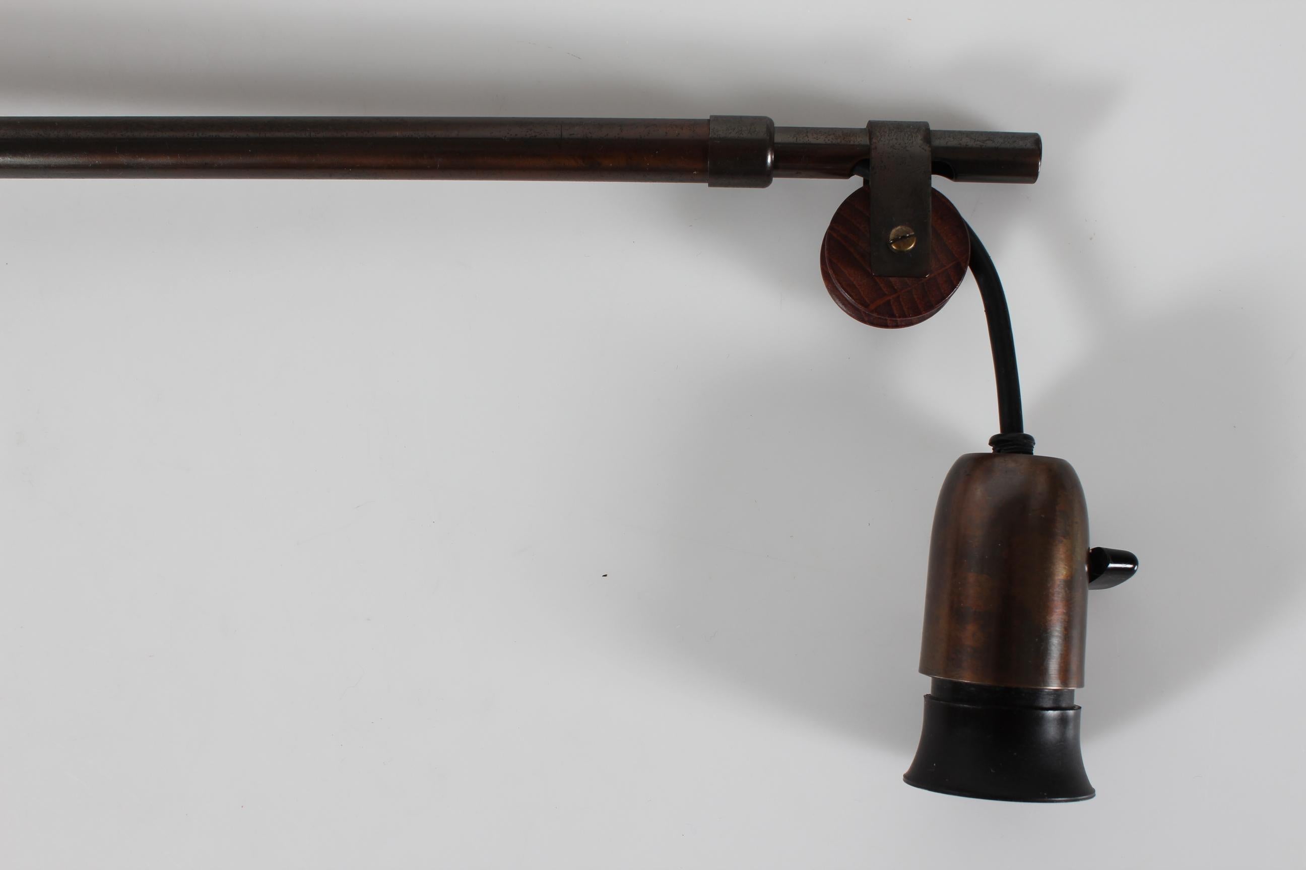 Lampada da parete vintage con braccio telescopico regolabile e ruota in legno nello stile del designer finlandese Paavo Tynell, probabilmente realizzata in Danimarca negli anni '30. 

La struttura dell'applique è in ottone con patina scura, montata