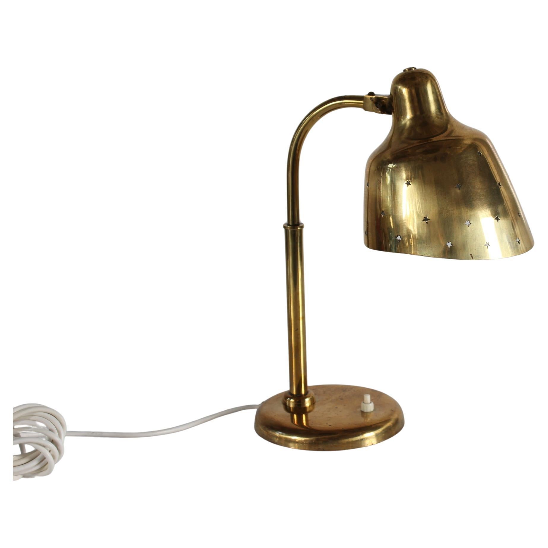 Lampe de bureau vintage en laiton dans le style du designer Vintage/One Paavo Tynell, fabriquée en Scandinavie dans les années 1930.

L'abat-jour en laiton taillé en biais présente un motif perforé de petites étoiles. L'intérieur de l'abat-jour est