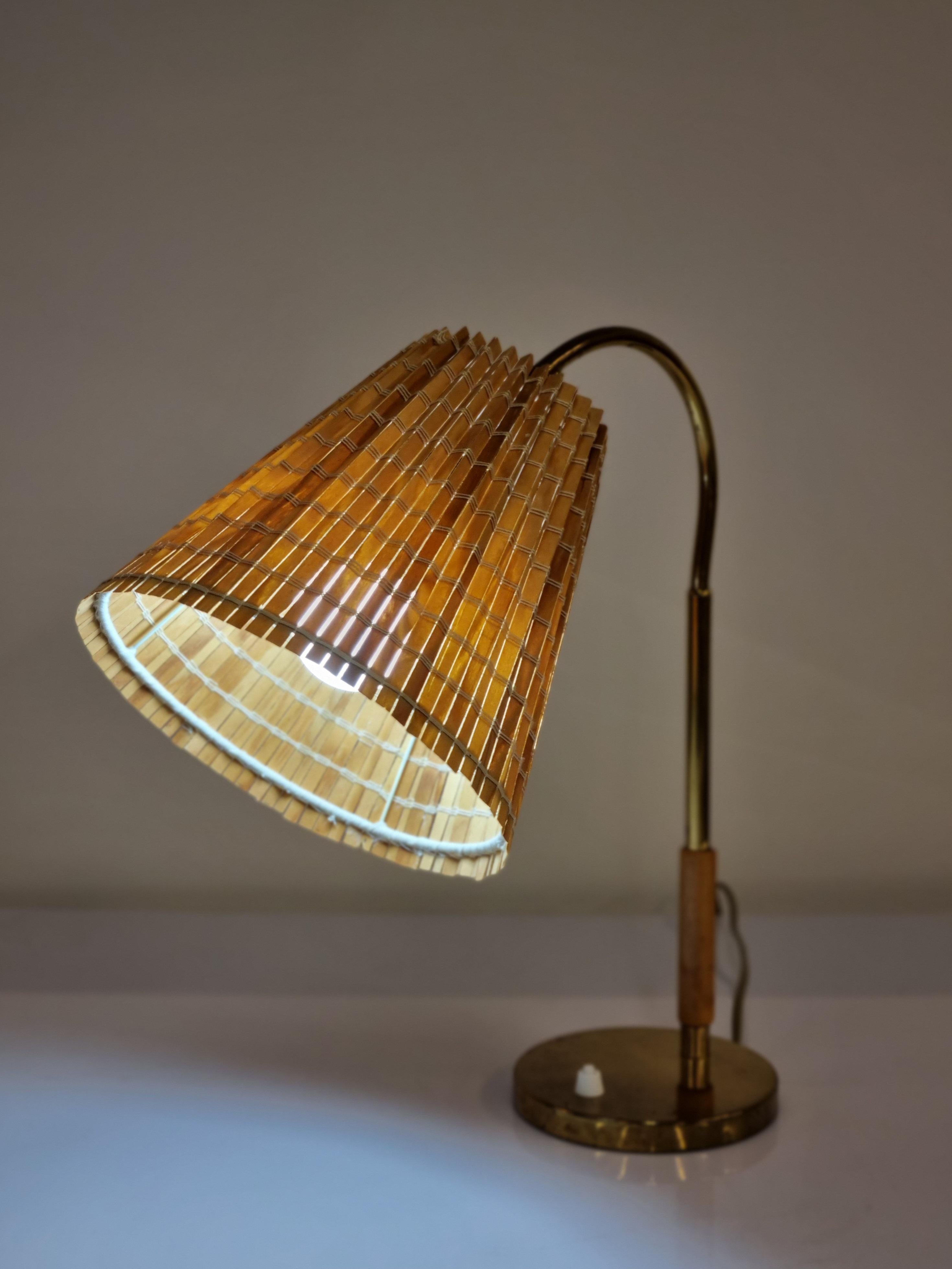 Paavo Tynell has designed this lamp model 9201 in the 1940s for Taito Oy.
This delicate table lamp has a brass body with a wooden handle part on the bottom of the tube. 
The adjustable wooden weaved shade is filtering light well. The electric wiring