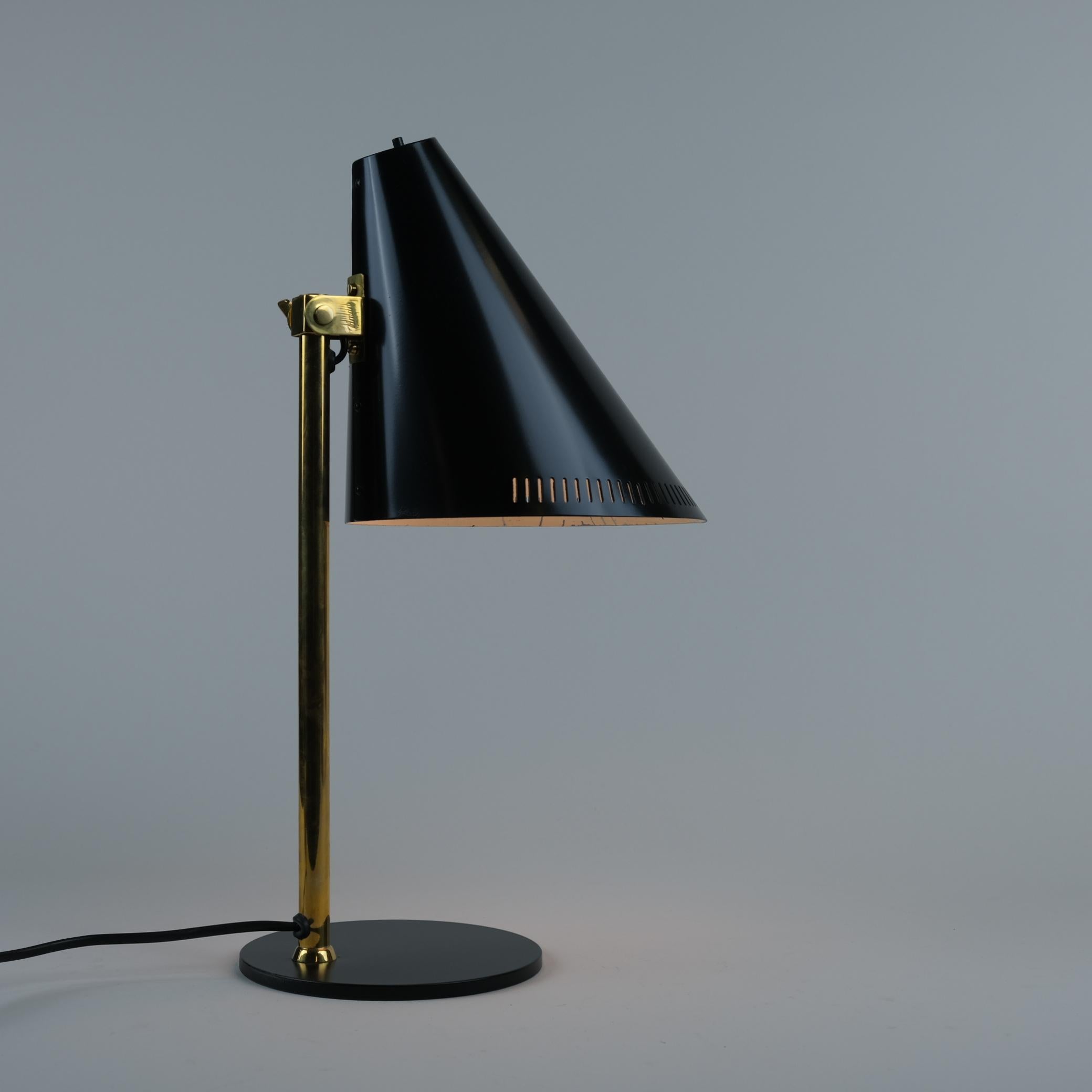 Cette lampe de table modèle H5-7 de Paavo Tynell est un modèle durable et pratique qui présente un mélange de 3 matériaux métalliques différents. Dans ce modèle, une tige ferme en laiton soutient un abat-jour conique en aluminium. L'abat-jour est