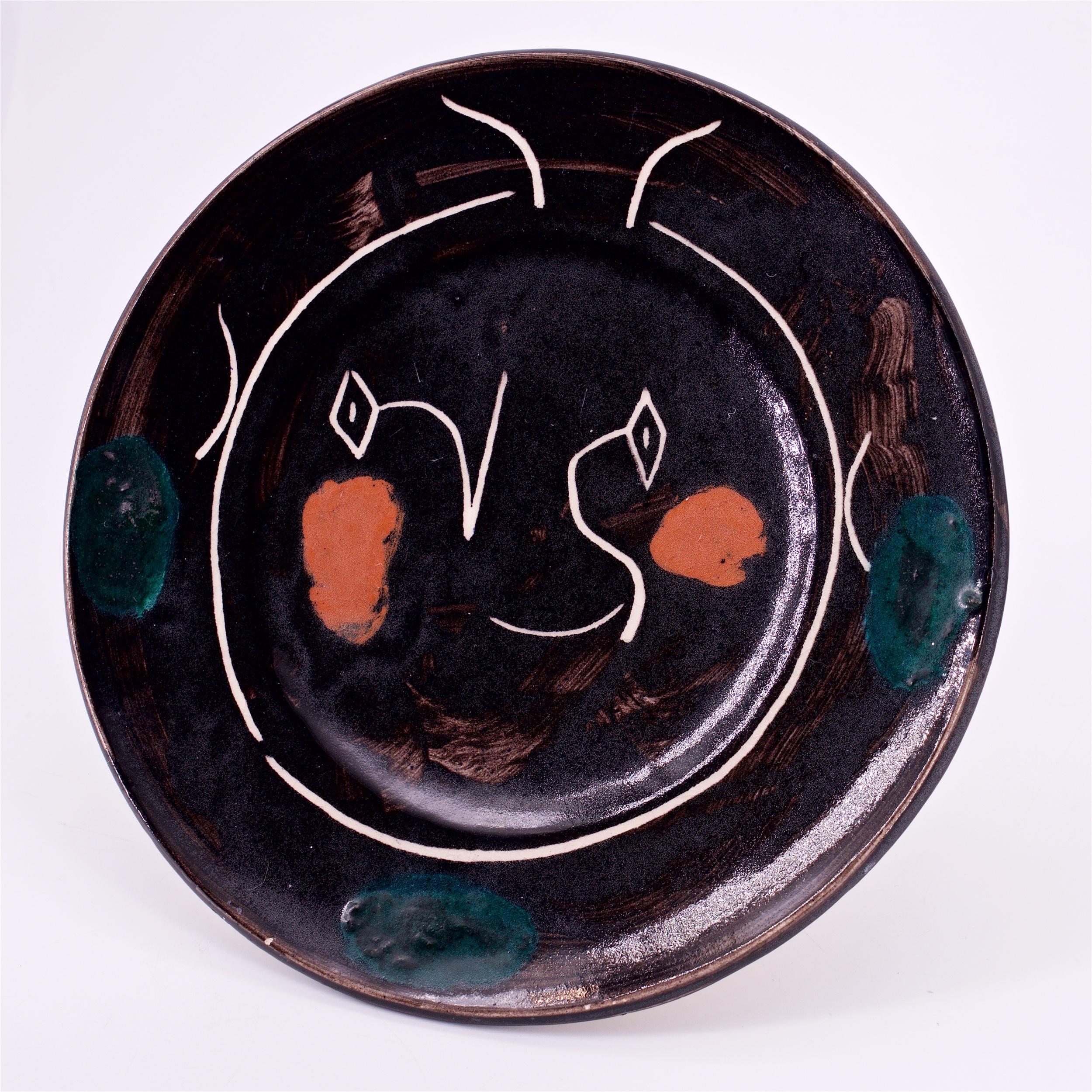 Black face service plate, glazed white earthenware, painted in colors; white, orange, and deep greys. Made in 1948, from an edition of 100, inscribed 'EDITION PICASSO' and 'B', with the 'Madoura PLEIN FEU' and 'EDITION PICASSO' pottery stamps on the