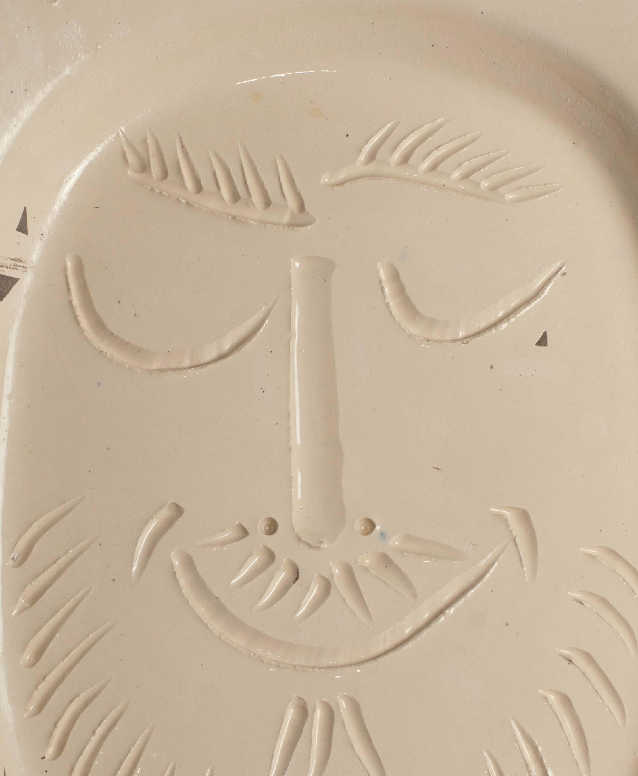 Original Picasso white dish showing a happy man’s face. Made white earthenware clay, knife engraved decoration under brushed glaze, grey patina. To a certain extent it is like minimal or zero-art, in a deep warm creamy color. Edition Picasso nr 114