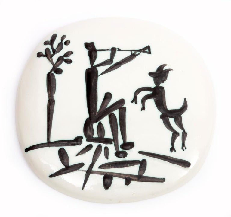 This Picasso ceramic plaque "Joueur de flûte et chèvre" is one in an edition of 450 and is made of white earthenware clay, engraving accentuated with oxidized paraffin, glaze bath. The piece is stamped on the underside 'Edition Picasso / Madoura