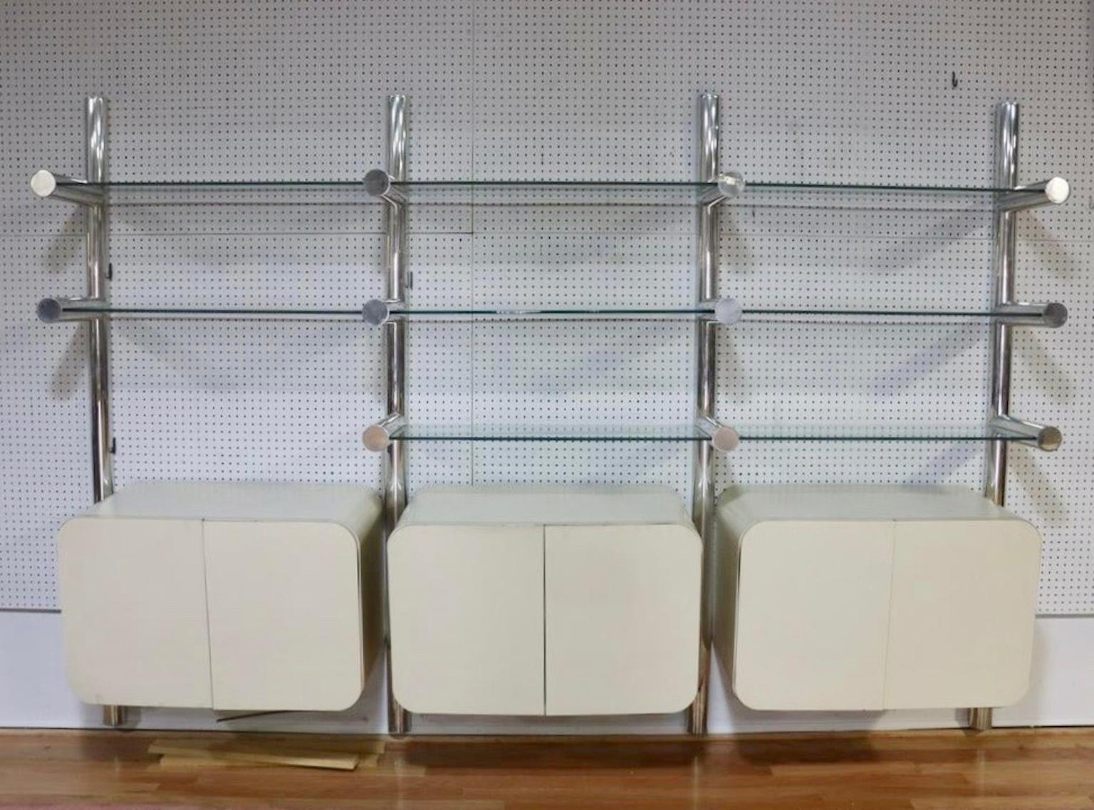 Pace collection ORBA wall system by Janet Schweitzer, 1974. Four extruded highly polished aluminum standards incorporating half inch thick glass shelves and three white laminate cabinets. Each cabinet is 35
