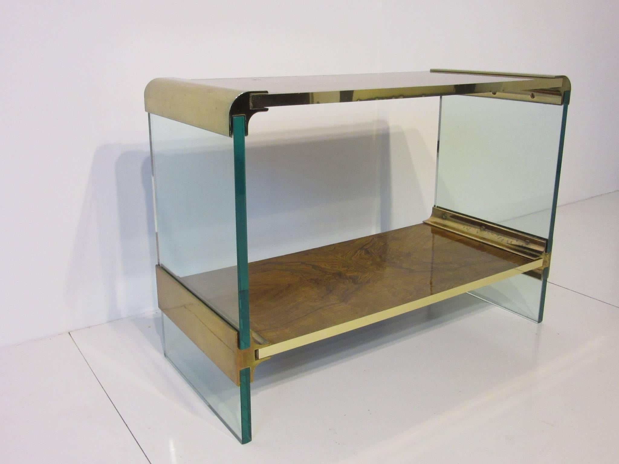 A rare smaller sized plate glass and brass console table with dark burl wood and brass trim to the front sides of the shelves. Manufactured by the Pace furniture company.