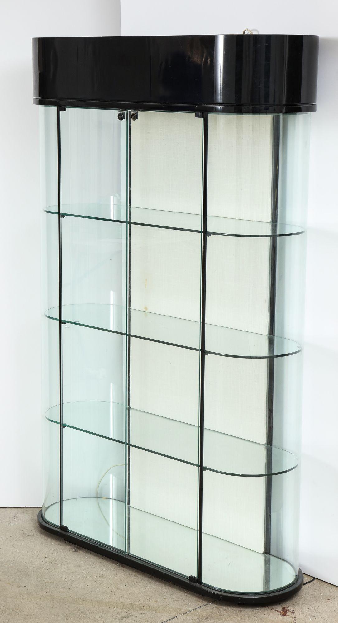 A useful and stylish modernist display cabinet by Pace with top interior spot lights and three glass shelves within a black lacquered curved frame and flanked by contoured glass panels either side of a pair of locking center doors.
Light surface