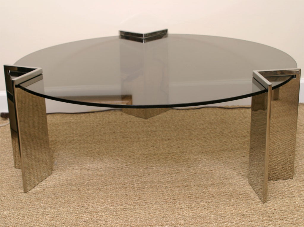 This sculptural round Leon Rosen for Pace cocktail table has 3 sculptural stainless steel bases that the clear glass fits into. The diameter of the glass is 52 inches. This is from the 1980s. It is modern, timeless and sculptural. The 3 angled bases
