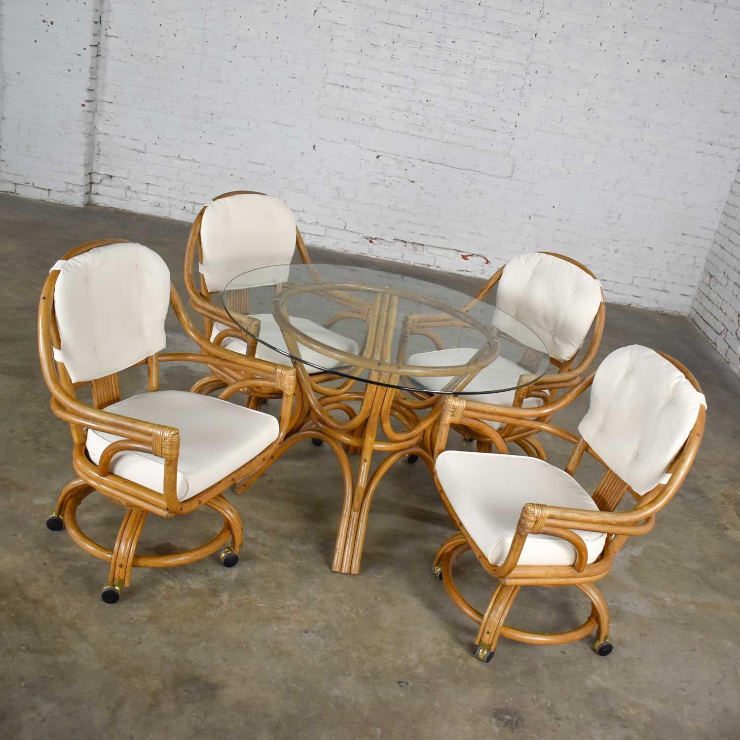 Beautiful game table or dining table set by Pacific Rattan of California including a round glass top rattan base table and four (4) swivel rolling rattan chairs with new off-white canvas zippered upholstery and removable seat and back cushions.
