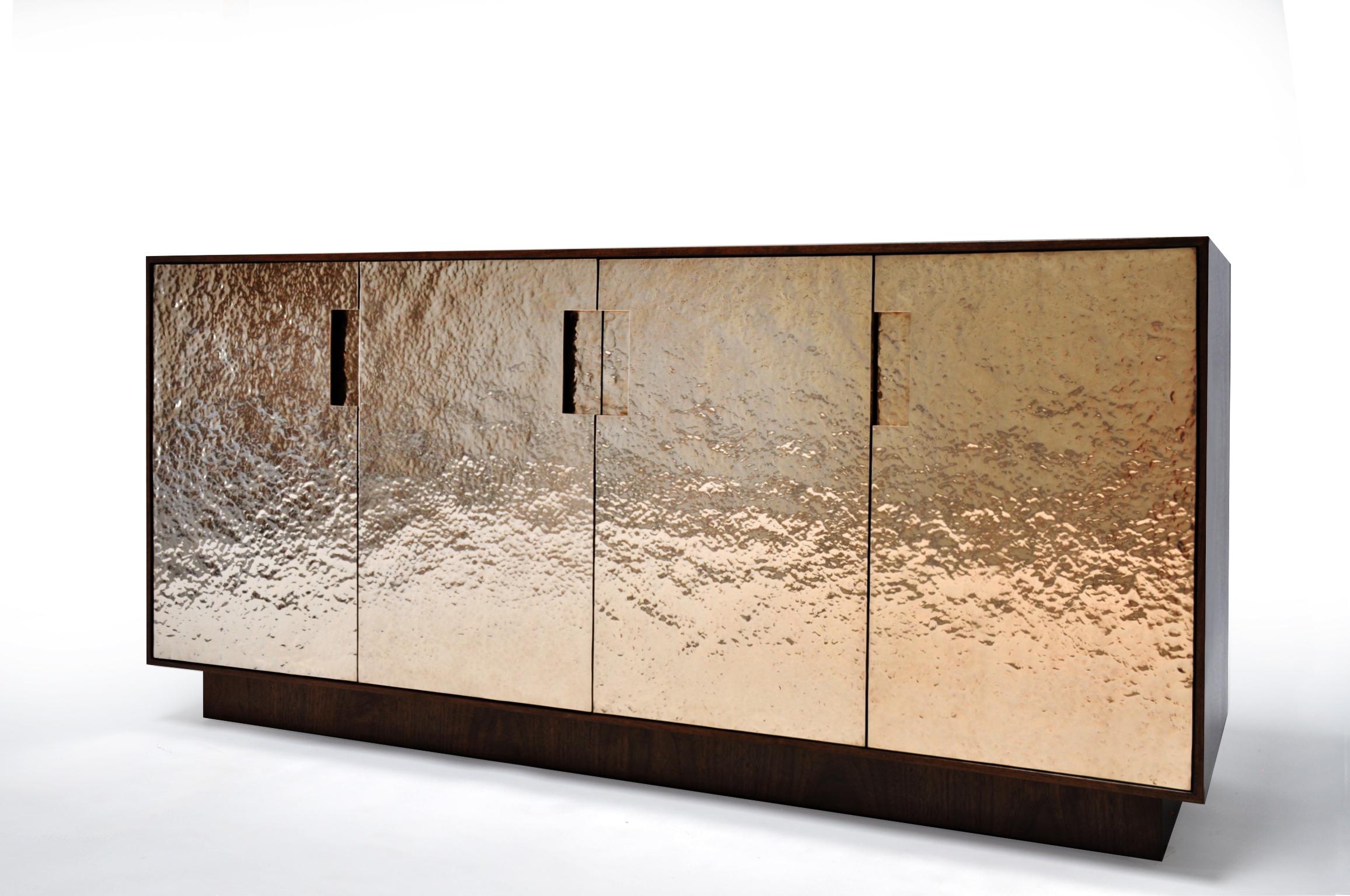 Pacifica cabinet in hammered bronze and walnut. Beautiful cabinet in luxurious Claro Walnut and hand hammered bronze doors.
Hand hammered bronze is a laborious process where the metalworker strikes bronze sheet thousands of times with a polished
