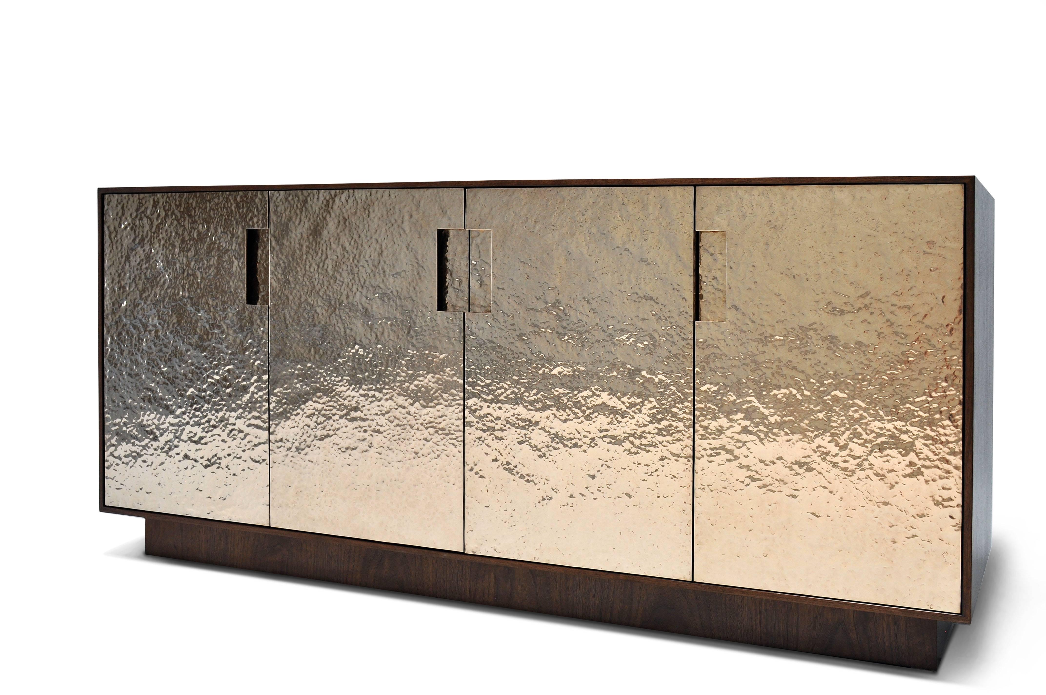 The Pacifica cabinet is created to be a quiet, but substantial presence. The cabinet, base, and interior are American Walnut. The interior configuration is adjustable shelves and drawers behind the doors. The bronze doors are hammered and formed by