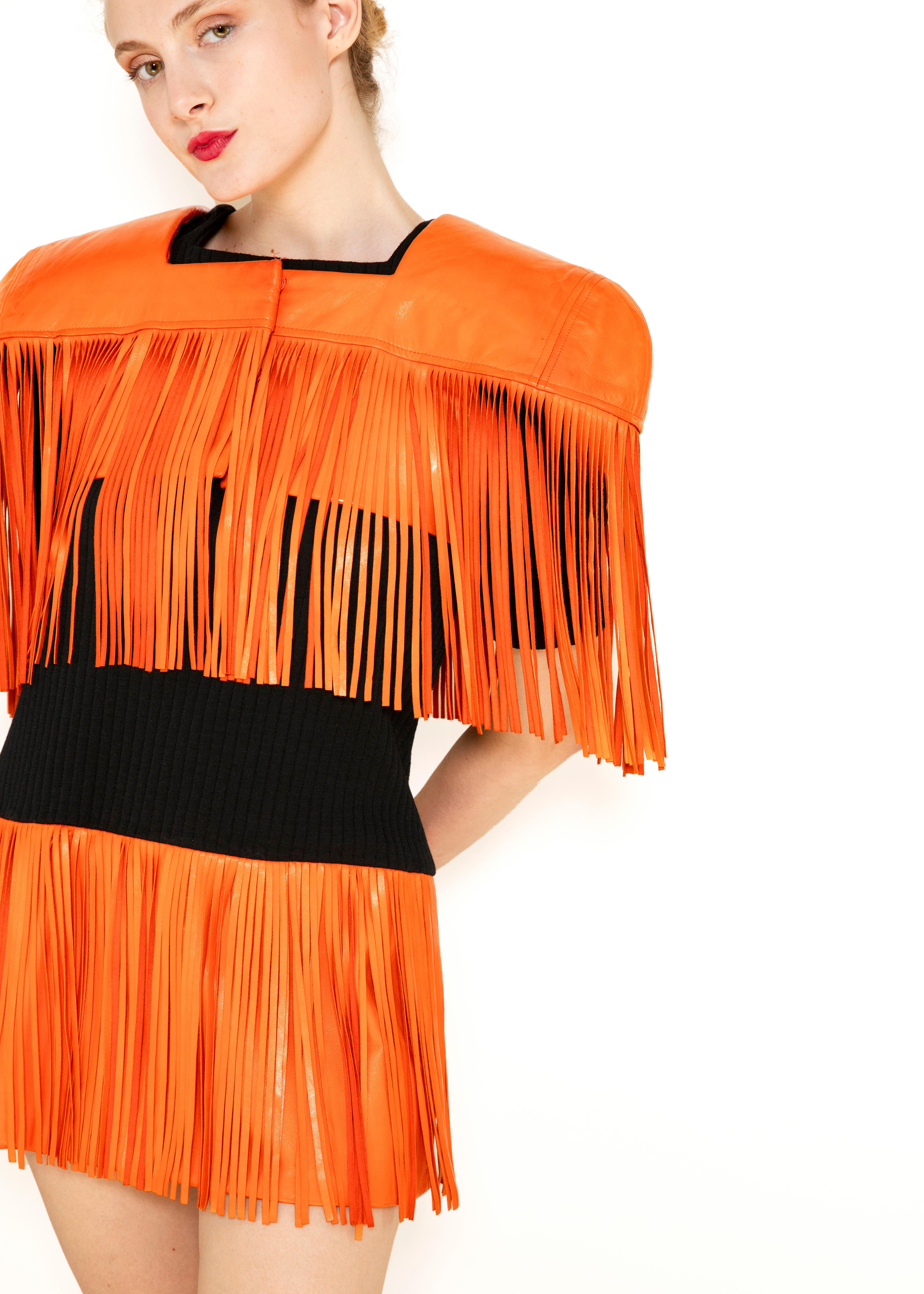 Unleash your inner risk-taker with the Paco Rabanne Leather Fringe Dress with Bolero. This bold dress features vibrant orange fringe and wide shoulders, perfect for making a statement. The micro dress is made of soft knit fabric, providing both