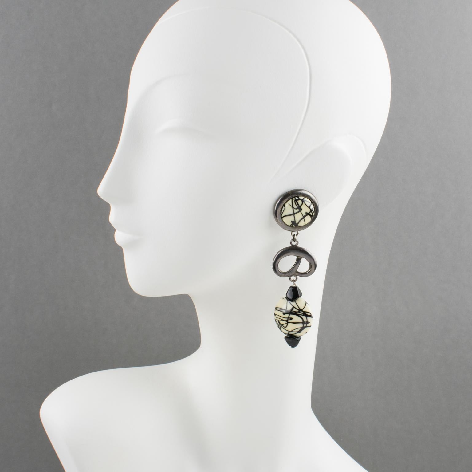 These stunning Paco Rabanne Paris clip-on earrings have a futuristic flair. They boast a long dangling-drop shape with metal in gunmetal color, all carved and see-thru, topped with resin cabochon and beads in black and white colors. Each piece is