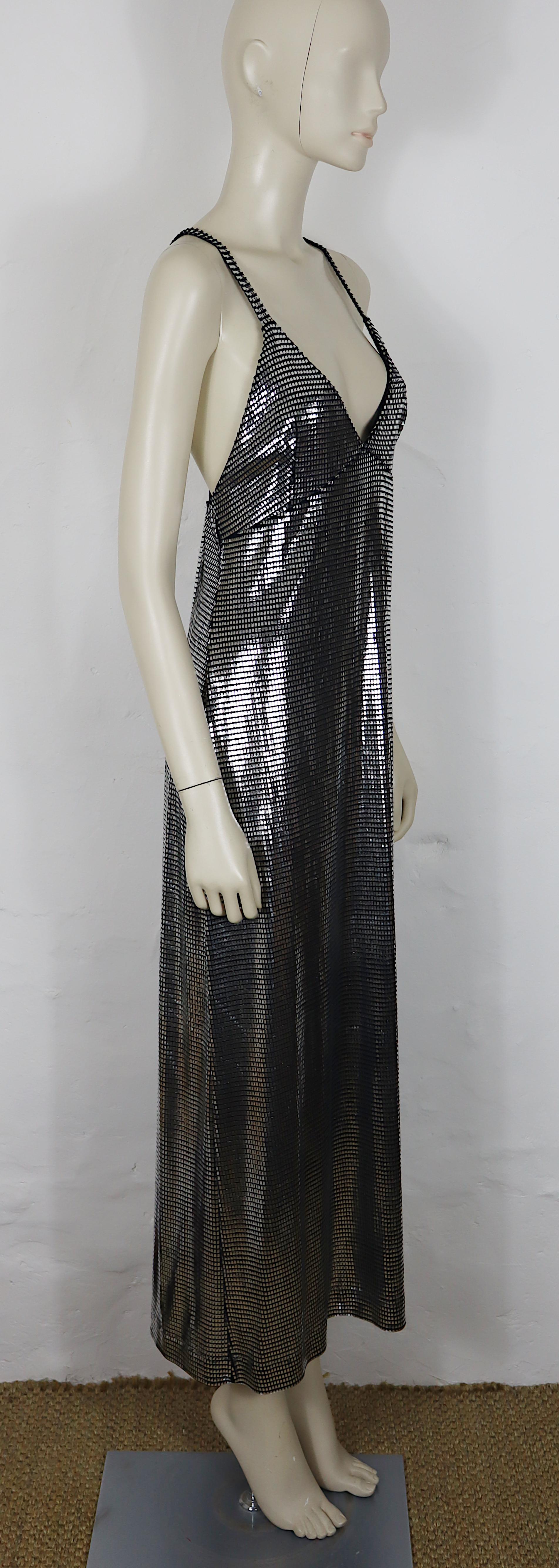 Das ärmellose Maxikleid von PACO RABANNE besticht durch seine silberne, mit Folie bedruckte Oberfläche, die ein metallisch schimmerndes Gitter erzeugt, das an Kettenhemden erinnert. Das Folien-Overlay ist auf einer schwarzen