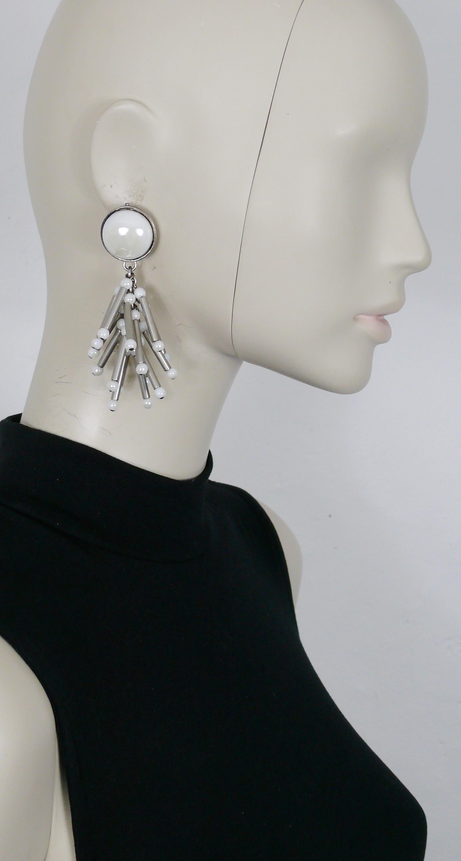Boucles d'oreilles pendantes PACO RABANNE en argent vieilli (clip-on) avec des breloques tubulaires embellies de perles en verre blanc et surmontées d'un grand cabochon en verre blanc.

Matériel métallique de couleur argentée.
Patine