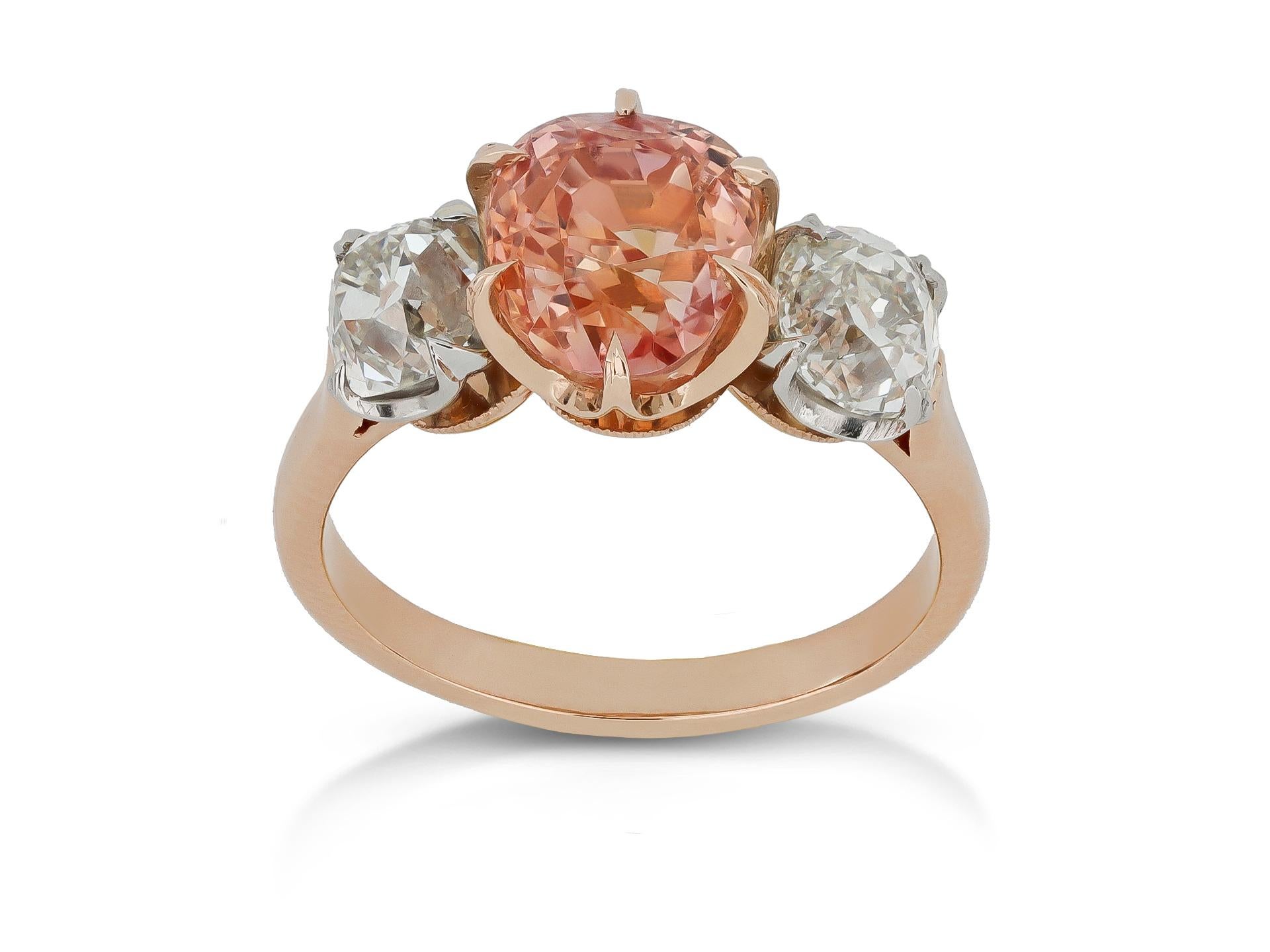 Bague à trois pierres en saphir de Ceylan padparadscha et diamant. Le centre est serti d'un saphir de Ceylan padparadscha naturel de forme coussin à taille mixte en serti griffe ouvert d'un poids de 3,11 carats, flanqué de deux diamants de mine