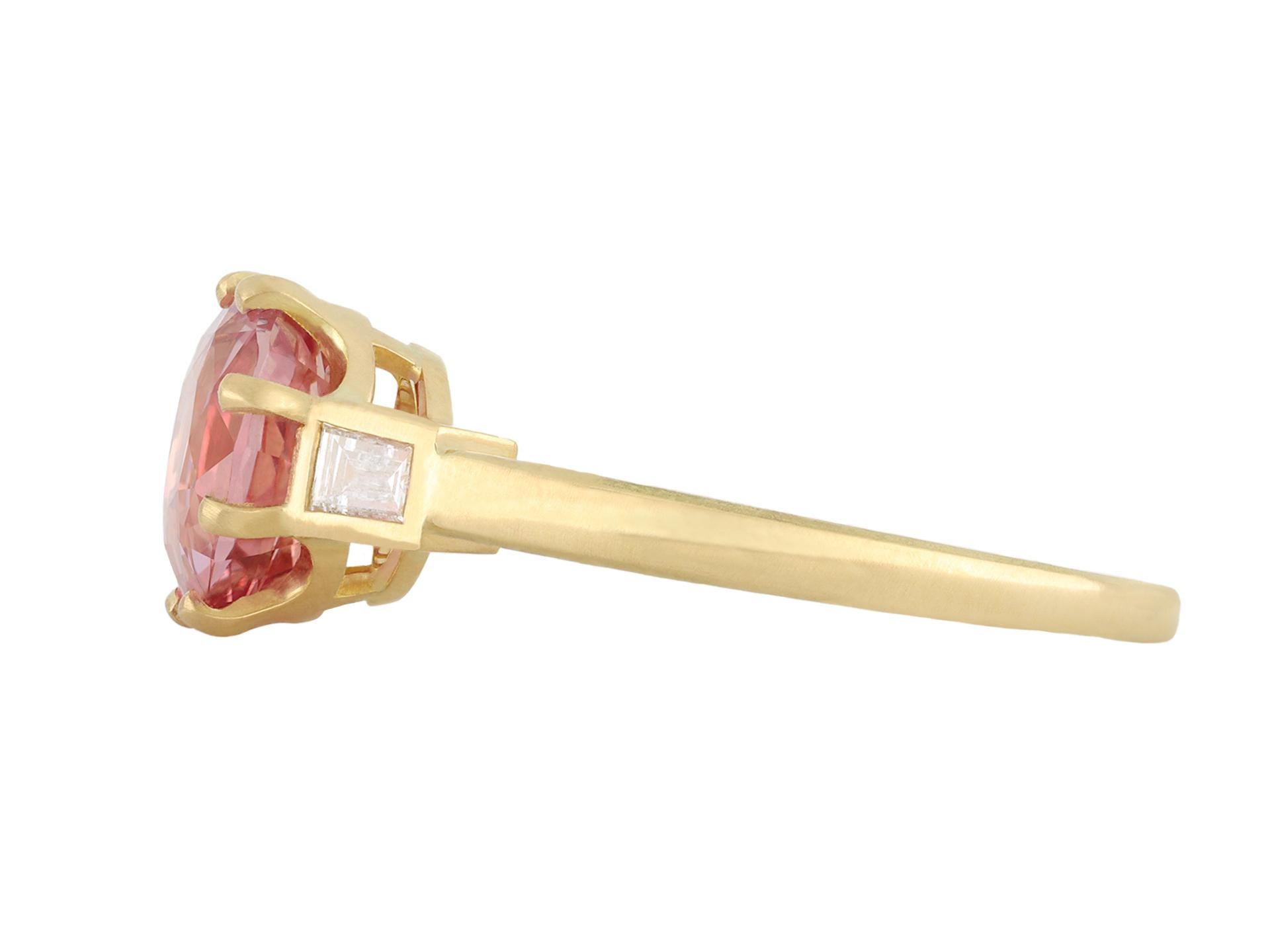 Padparadscha sapphire and diamond flanked solitaire ring. Set to centre with an oval double brilliant cut natural unenhanced Padparadscha Madagascan sapphire in an open back claw setting with a weight of 2.07 carats, flanked by two rectangular