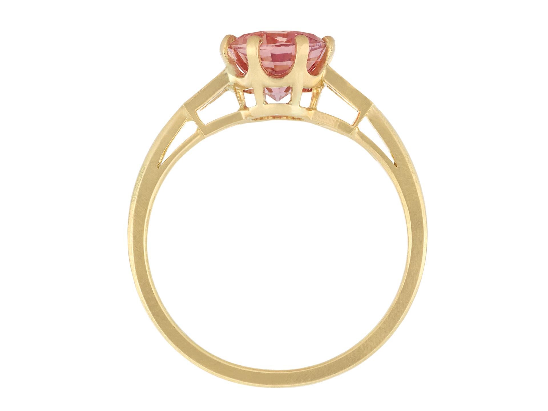 Oval Cut Padparadscha sapphire and diamond flanked solitaire ring, circa 1990. For Sale