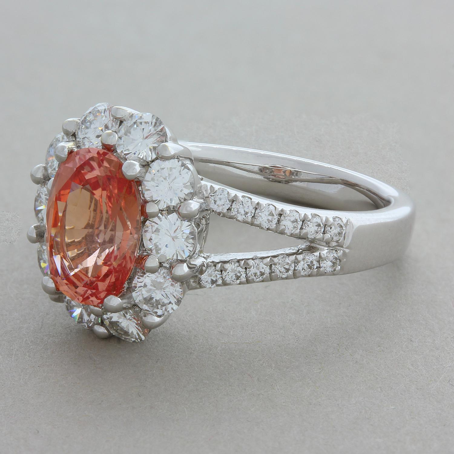A summer evoking GIA certified Padparadscha sapphire weighing 2.16 carats with a rich lotus flower color takes center stage of this lovely ring. It is accented by 1.40 carats of round brilliant cut diamonds that halo the rare sapphire and run along