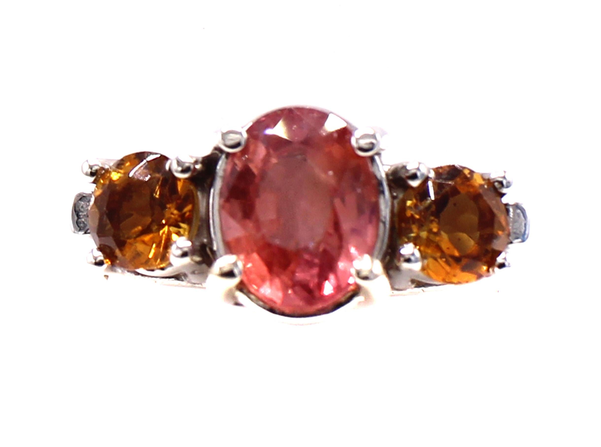 Uno splendido zaffiro Padparadscha di 2,15 carati è il pezzo centrale di questo coloratissimo anello con tre pietre. Gli zaffiri Padparadscha sono tra gli zaffiri più rari che si possano trovare e il loro colore unico, con una distinta tonalità