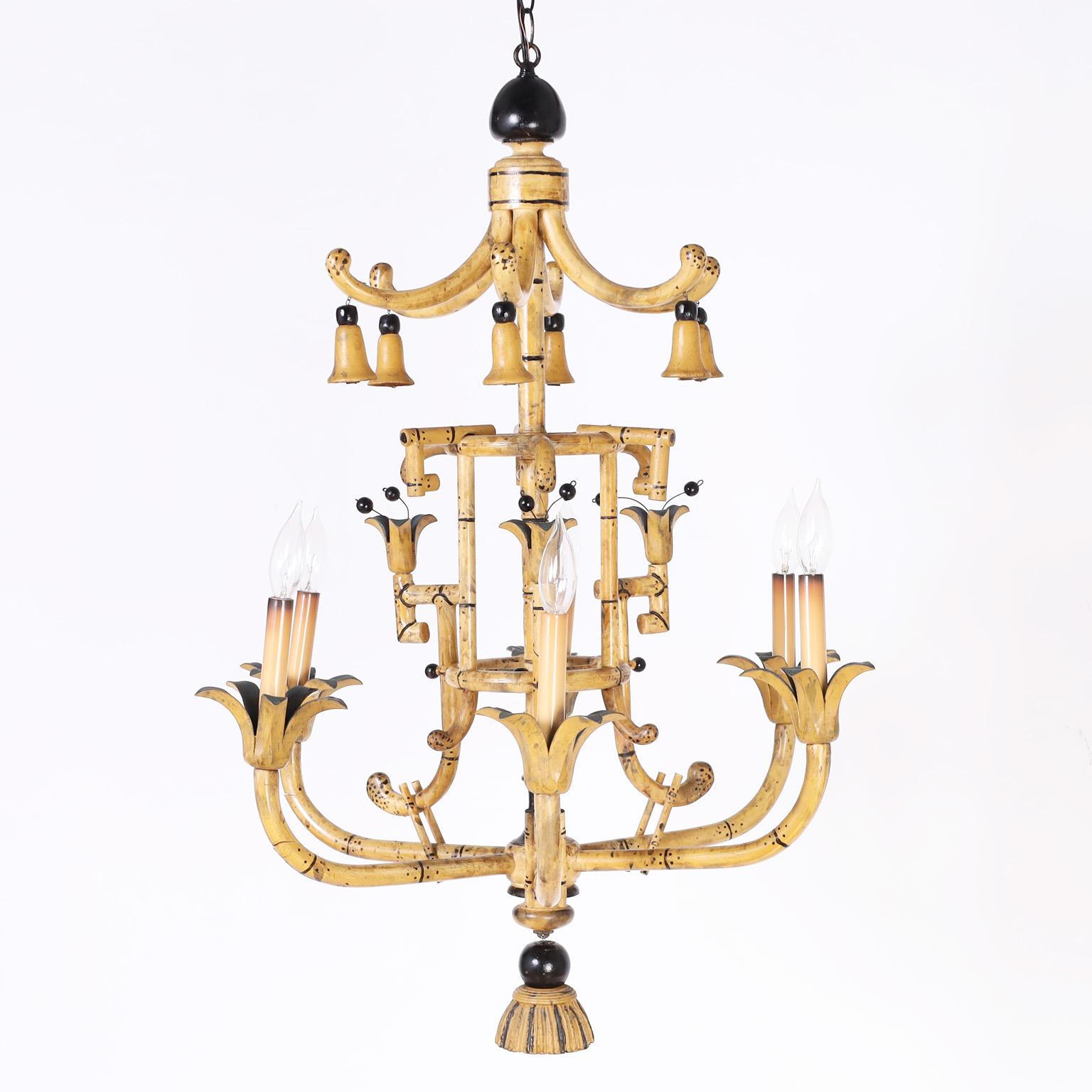 British colonial style six light faux bamboo chandelier crafted in wood with a pagoda style top having tassels, center section with flowers, six arms with floral candle cups, and finished with a wood tassel at the bottom.