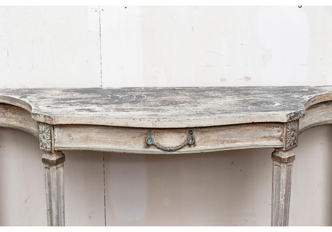 A particularly Stylish Tiered Console in a sophisticated worn paint finish. A shaped console table in a greenish-gray and off white antique type painted finish with some gilt details. The frieze with a drawer and a verdigris metal pull with torches,