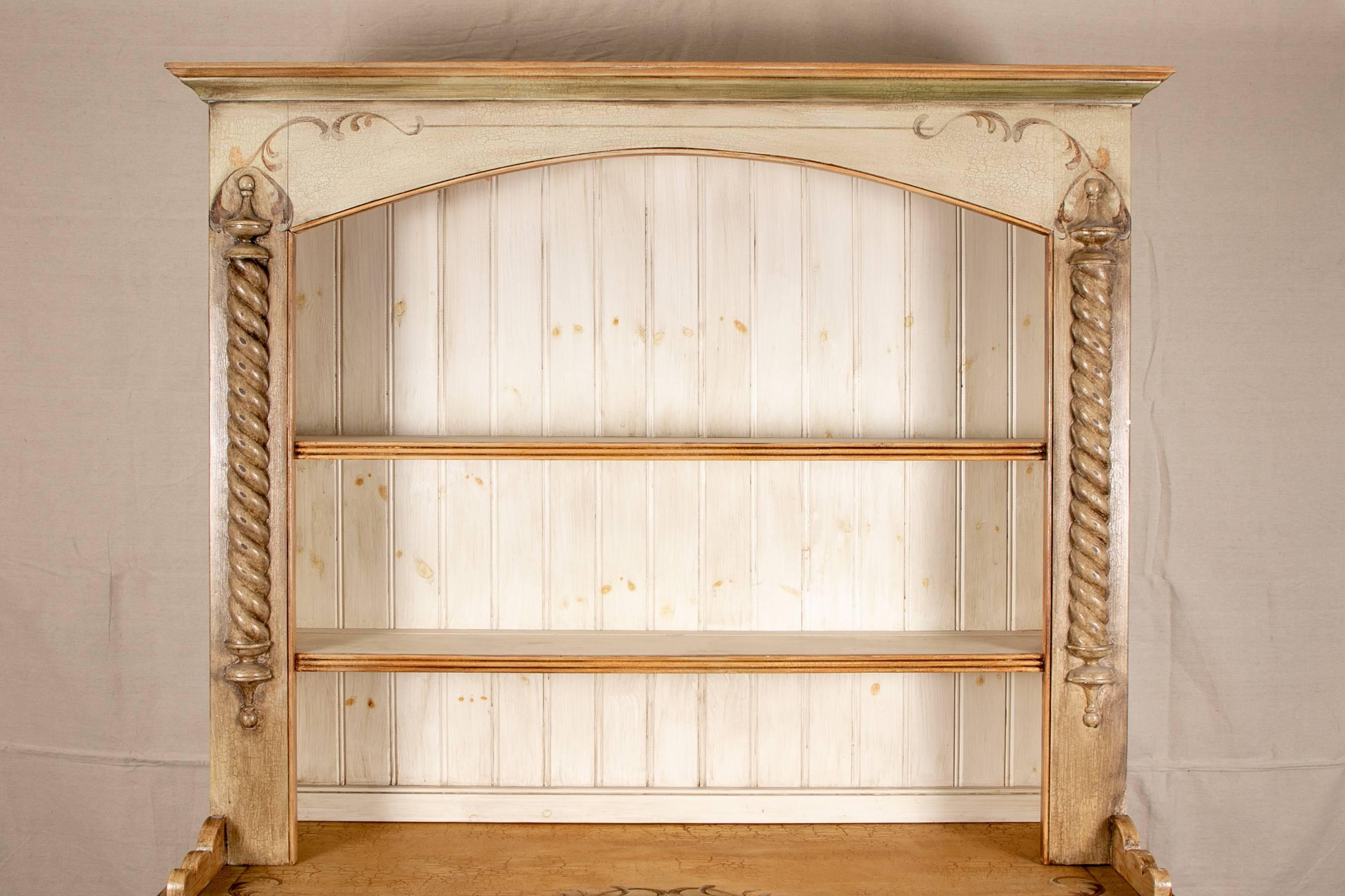 Paint decorated cupboard, overhanging cornice over the cabinet with barley twist supports and two open shelves, the lower part with barley twist supports and three short drawers over three doors decorated with leaves with key holes (with a key)