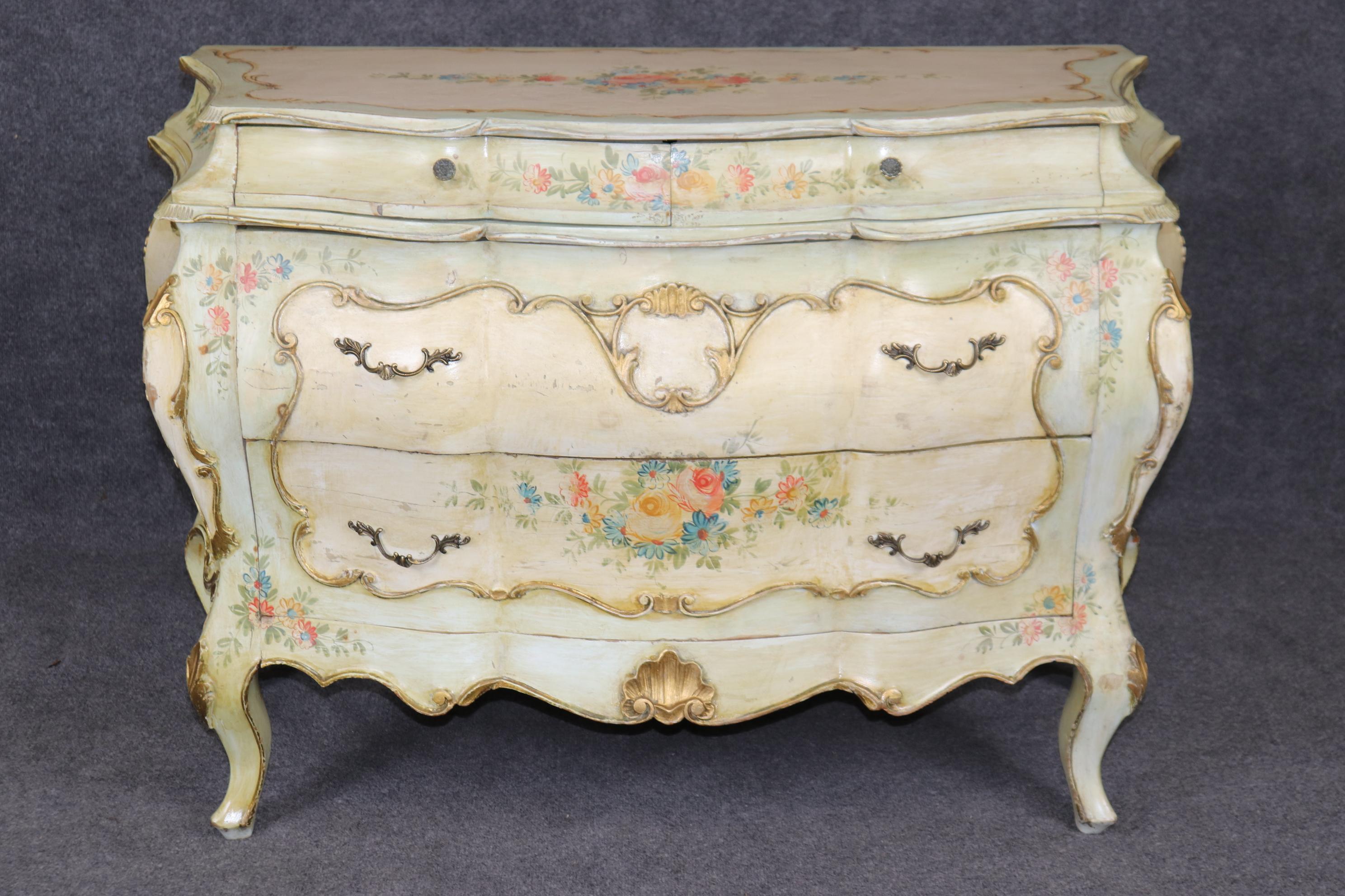 This is a charming and beautifully paint decorated bombe Venetian commode from teh 1940s era and in subtle pastel hues with flowers adorning most of the surfaces. The commode is in good original condition and will show some distressed areas from age