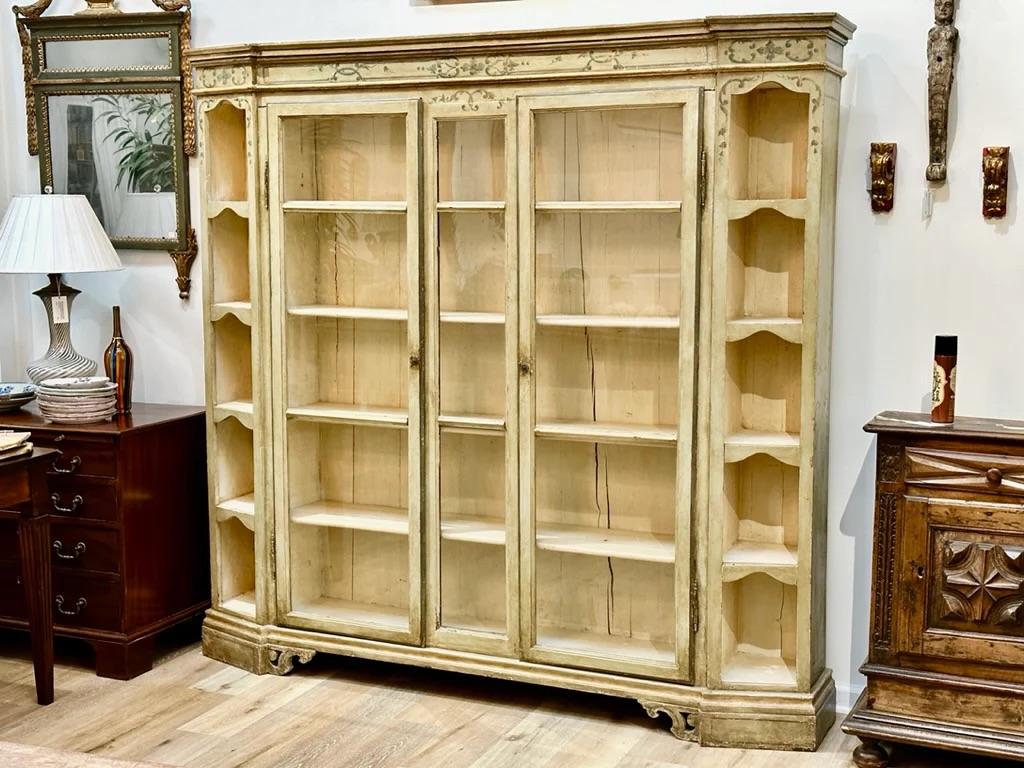Early 19th Century Danish bookcase, The graduated 5-sided cornice over a pair of glazed doors, having five shelves and pale green polychrome, flanked by 5 cubbyholes to each side, the feet with a scrolling flourish. 78.5” h. x 83” w. x 13” d.
