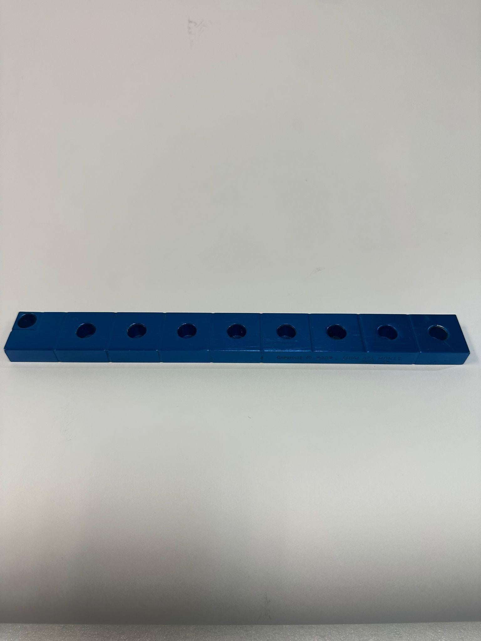 This minimalist Hanukkah lamp created in 2002 by the Italian designer Luigi Del Monte, is made of painted aluminum in a striking blue finish. The lamp’s design features a linear arrangement of eight modular rectangular blocks, each with a hole for