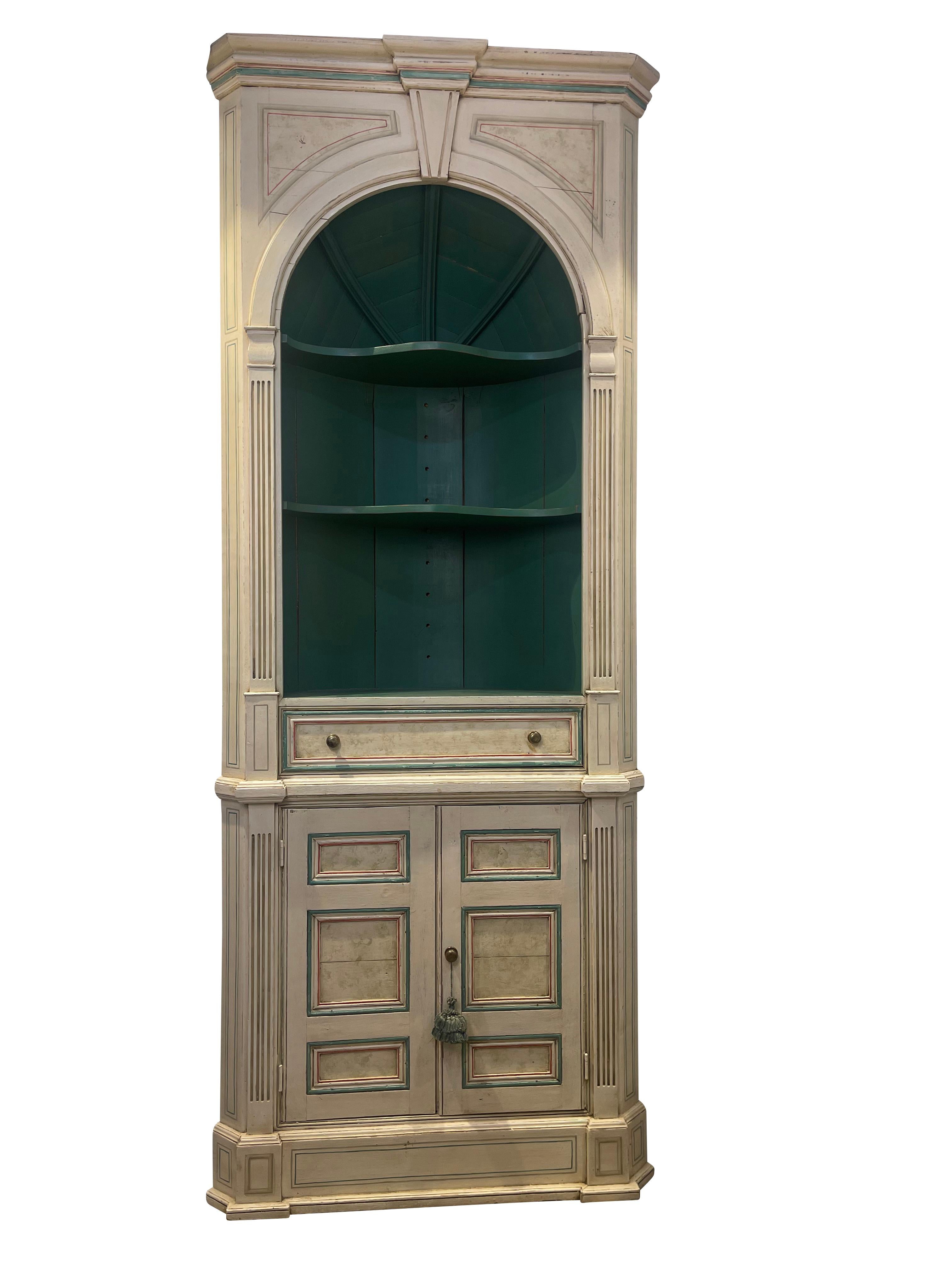 20th century neoclassical painted corner cabinet ~ bookcase that has a splendid European feel. The mitered corners project the piece out into the room, yet its impact on the floor plan is minimal due to utilizing otherwise unused corner space.