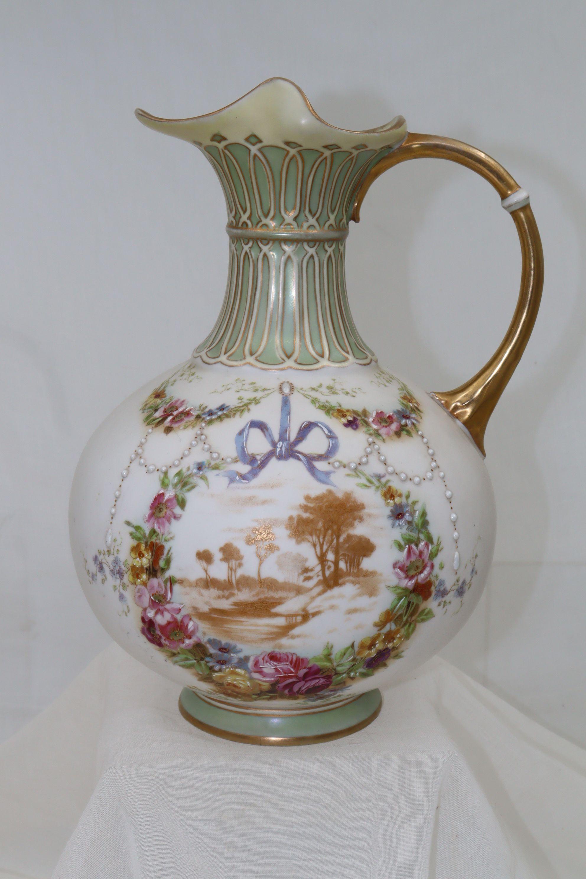 This very pretty painted and gilded parian pitcher is decorated with hand painted ribbons, swags of jewelled and highlighted flowers and strings of jewelled pearls. In the centre is a rural scene, printed in gold and encircled by a cartouche of hand
