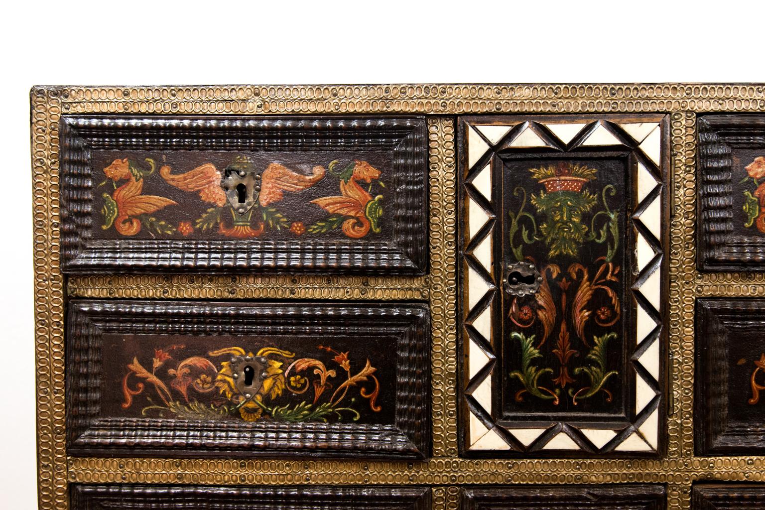 Bemalter und eingelegter italienischer Schrank auf Ständer, mit Buchsbaum-, Nussbaum- und Knocheneinlegearbeiten, die Oberseite mit geometrischem Muster eingelegt, die bemalten Schubladen mit geprägtem Messing ummantelt, die mittlere Tür offenbart